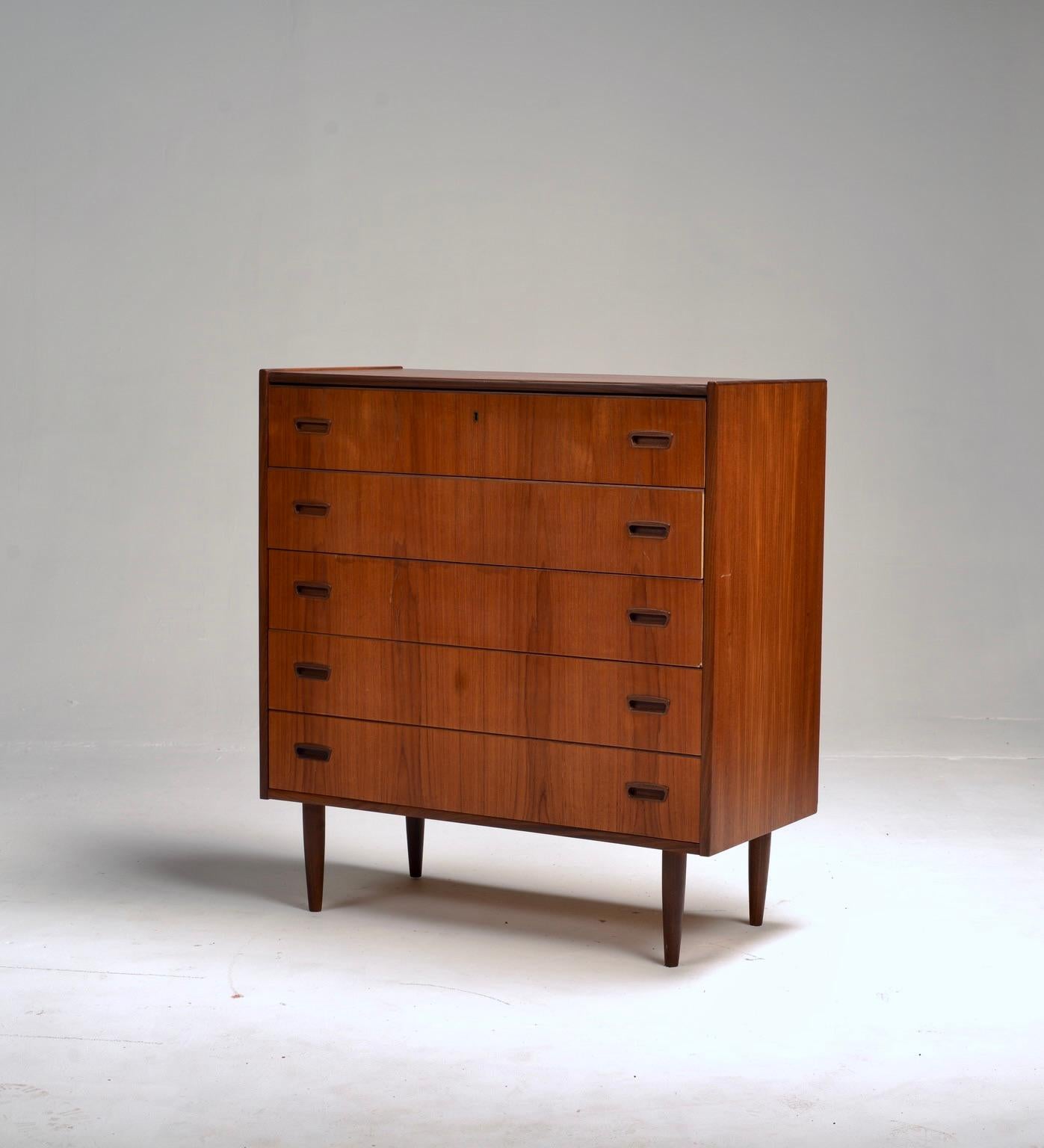 Comò classico in teak massiccio della metà del secolo scorso. Questo bellissimo comò a cinque cassetti è intramontabile nel design e nei materiali, con linee pulite e moderne e un teak ricco di venature. I cassetti scultorei e le gambe affusolate