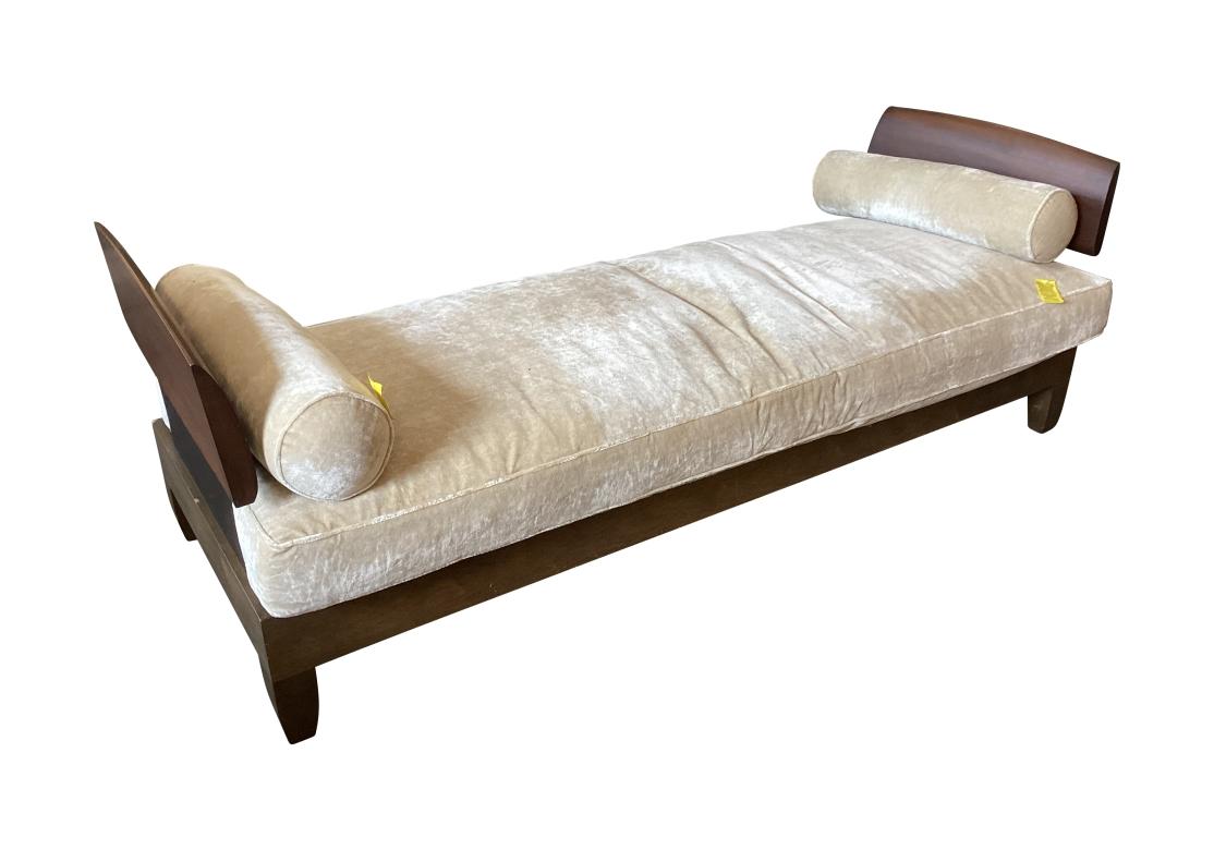 A long rectangular modernist style daybed with tall shaped wood sides with black laminate panels below. The lower wood frame raised on square shaped legs. A fine quality upholstered seat cushion and a pair of bolsters in a pale fabric. The classic