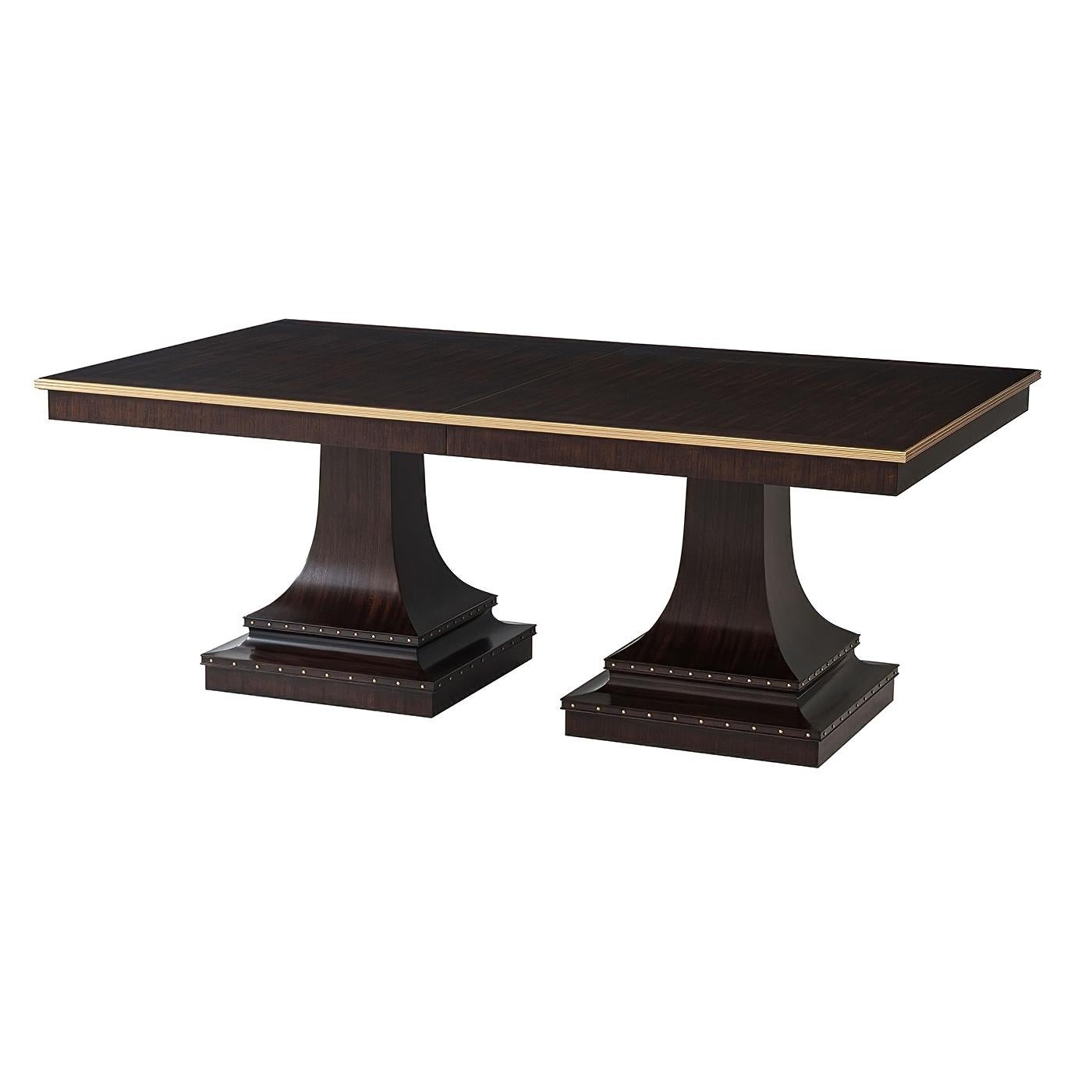 A modern Italian classically inspired dining table. The extendable dining tabletop in Mahogany veneer is detailed with a Brass reeded edge. Two down-swept and tapered monolithic pedestals form the molded base, decorated with brass nailhead trim – a