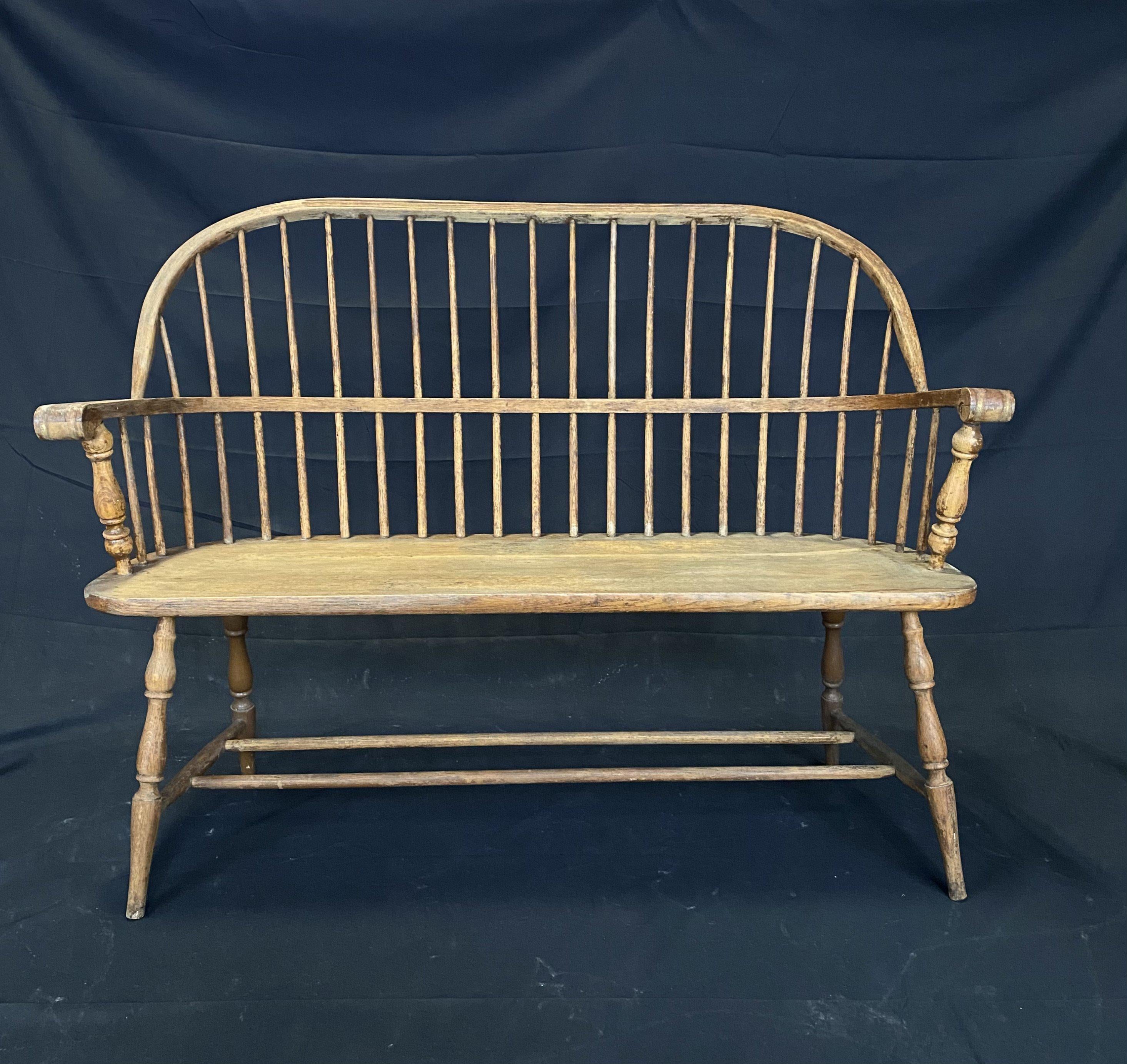 An original Windsor 19th century painted hoop spindle back oak bench with an arched back having turned slats, arms and uprights, the shaped plank seat above turned splayed legs. Remnants of early brown paint are visible. Bought in Maine. Solid and