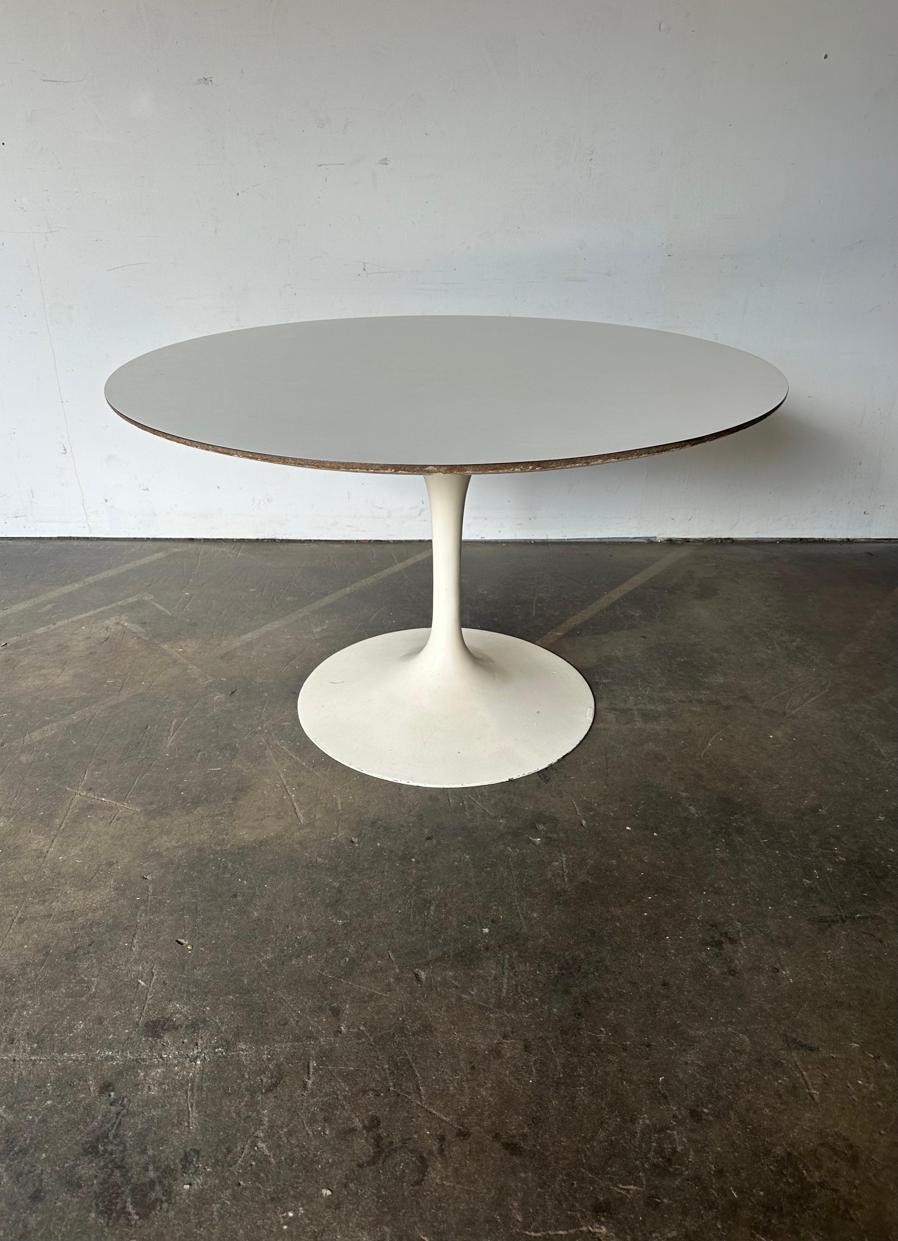 Gorgeous, classic authentic edition of the iconic Knoll tulip dining table. Designed by Eero Saarinen, executed in cast iron base and white laminate knife edge top. Early heavy single cast iron base. Signed with early Knoll bow tie label under the