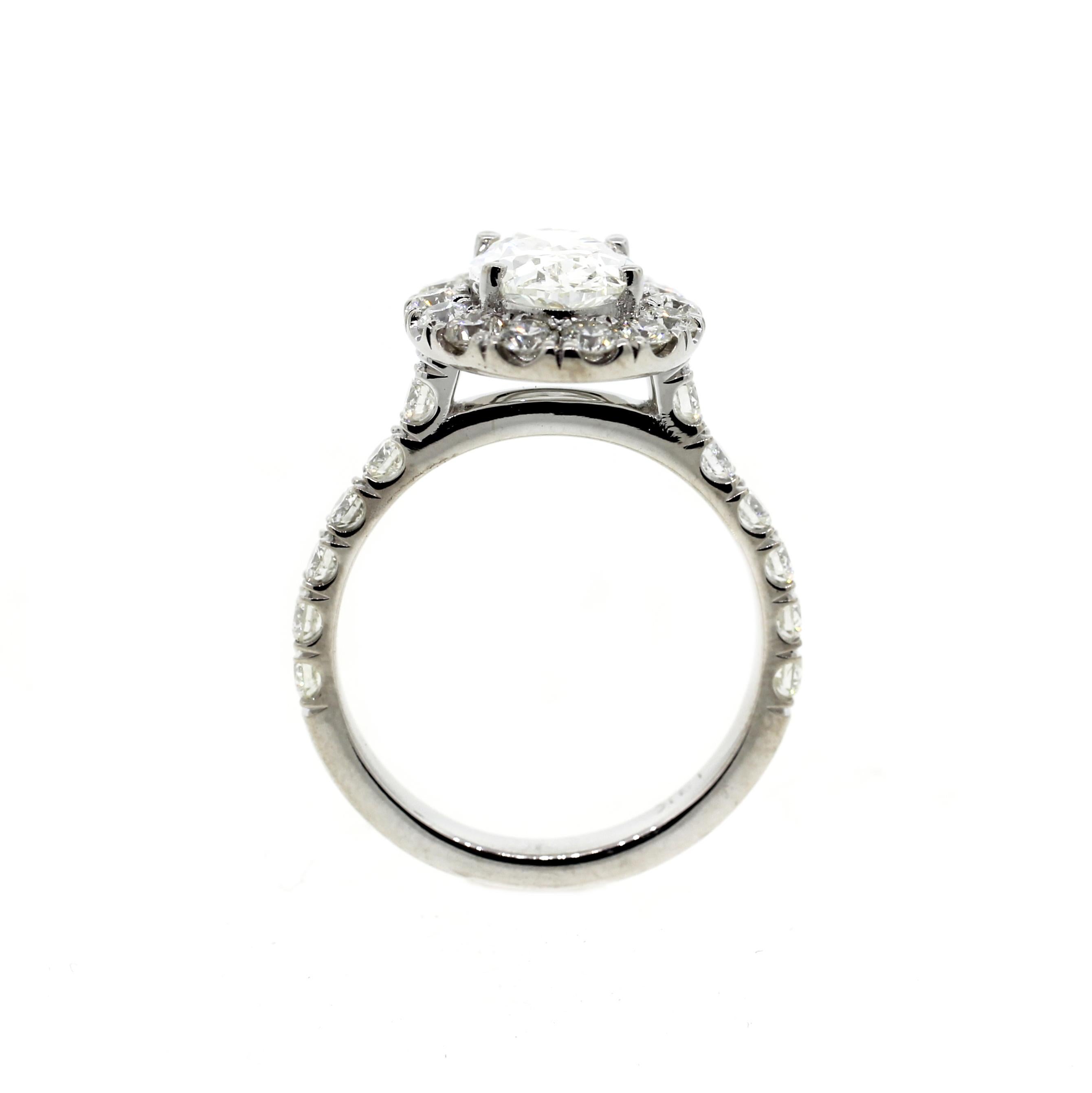 This classic oval shaped diamond engagement ring features a 1.25 oval shaped center stone surrounded by a larger than usual diamond halo. Set in 18K white gold with diamonds on the shank with a built-in (raised) cathedral setting. The matching