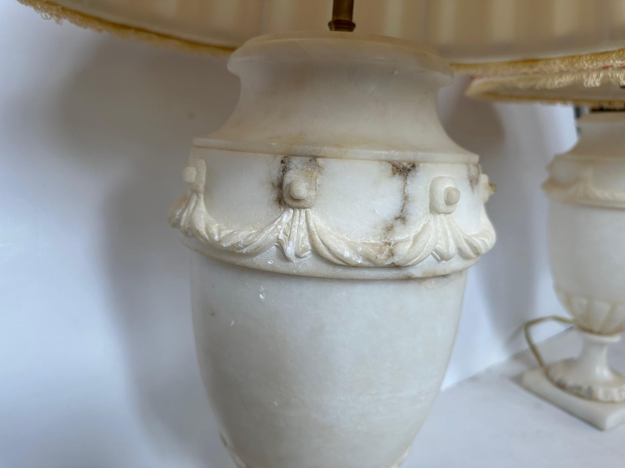 Elegant sculptural pair of urn shaped alabaster table lamps having pretty wreath decoration around the periphery and silk shades.
Shade: 12.25” H x 12” W top.