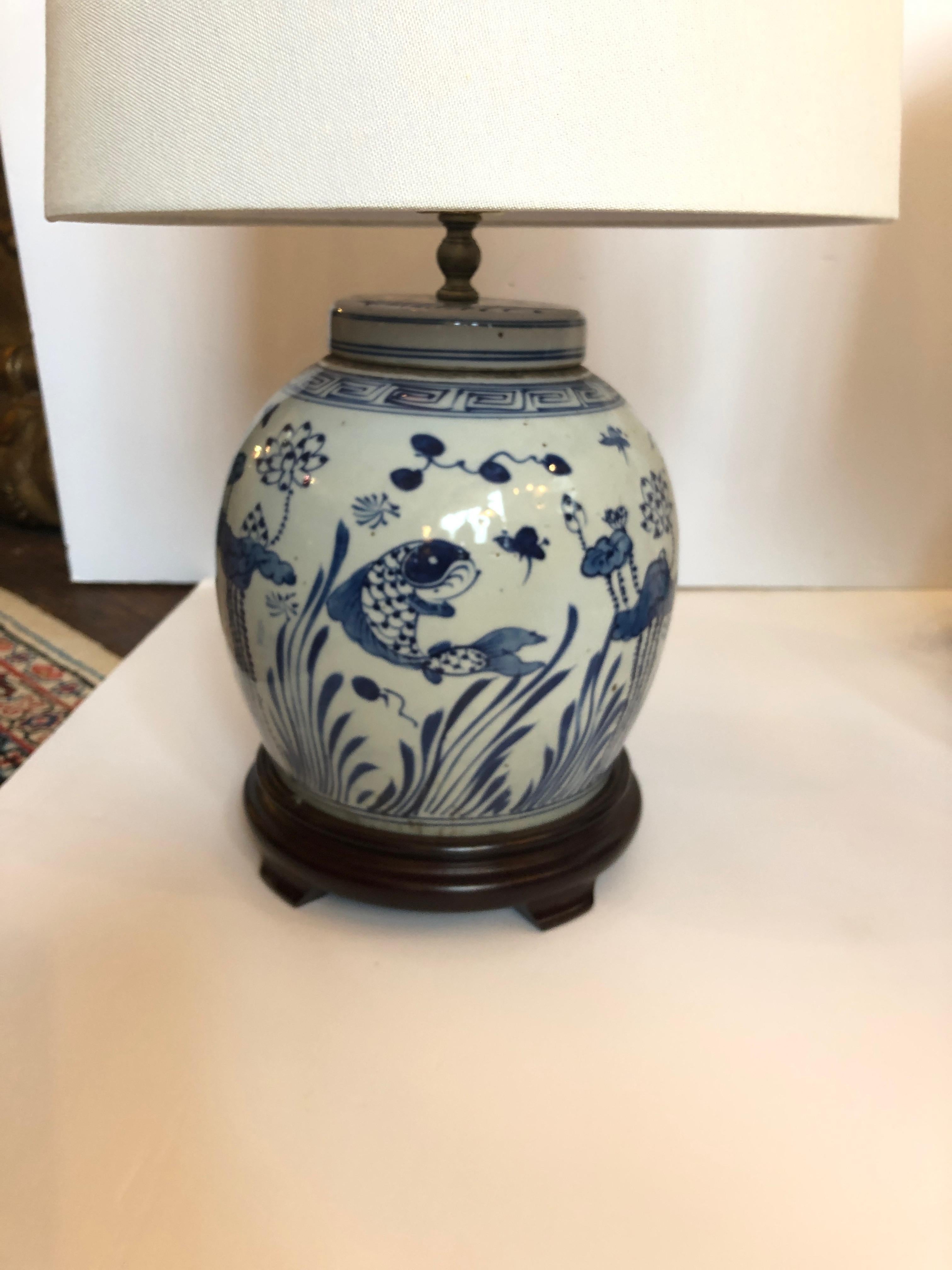 Elegant pair of blue and white canton style ginger jars mounted as lamps on dark wood stands and decorated beautifully with foliage and carp fish. Jars are 10 W bases are 8.5.