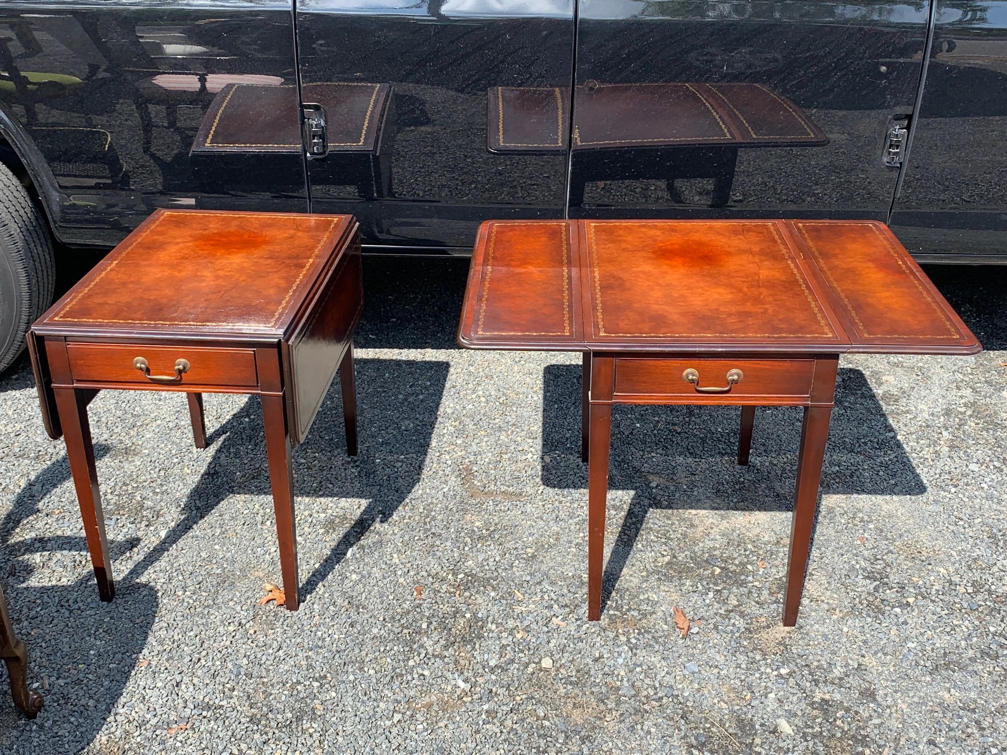 Handsome pair of pembroke drop leaf end tables having rich tooled leather tops and single drawers. With sides extended Measures: 36.5 W 27 D 25 H.