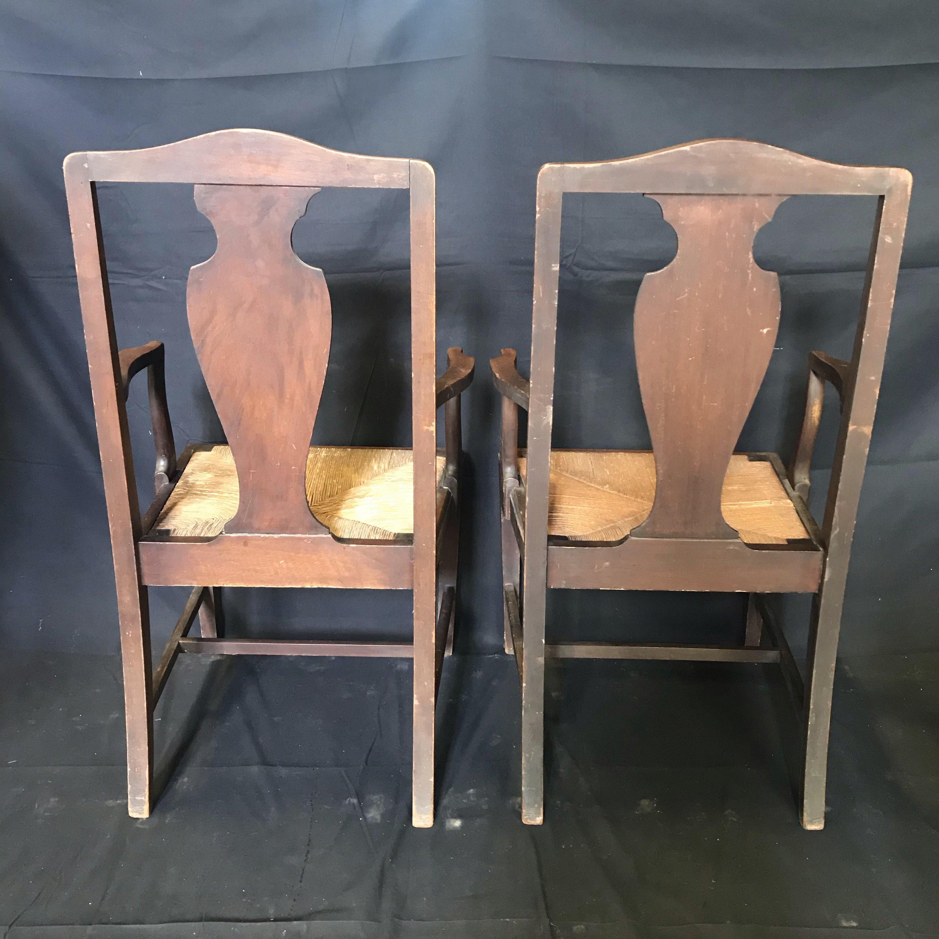 Very handsome set of two early British armchairs in Chippendale style with solid urn-shaped back splats and turned front legs with stretchers. They retain their original finish and rush seats in good shape, and are in very fine vintage condition,