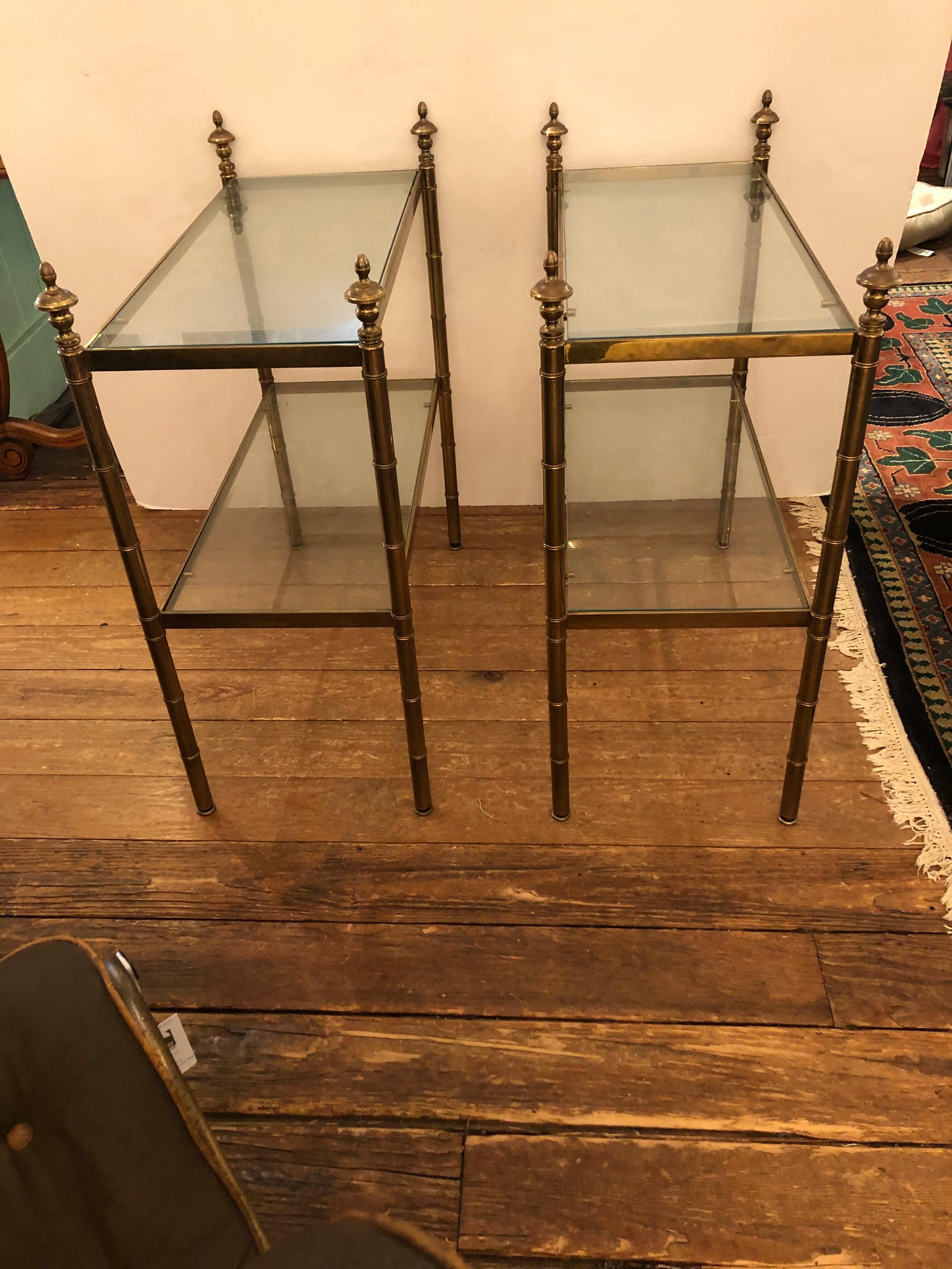 Refined and classic pair of two tier brass and glass end tables having handsome finials and great functional use for display and storage with a clean floating tailored look.