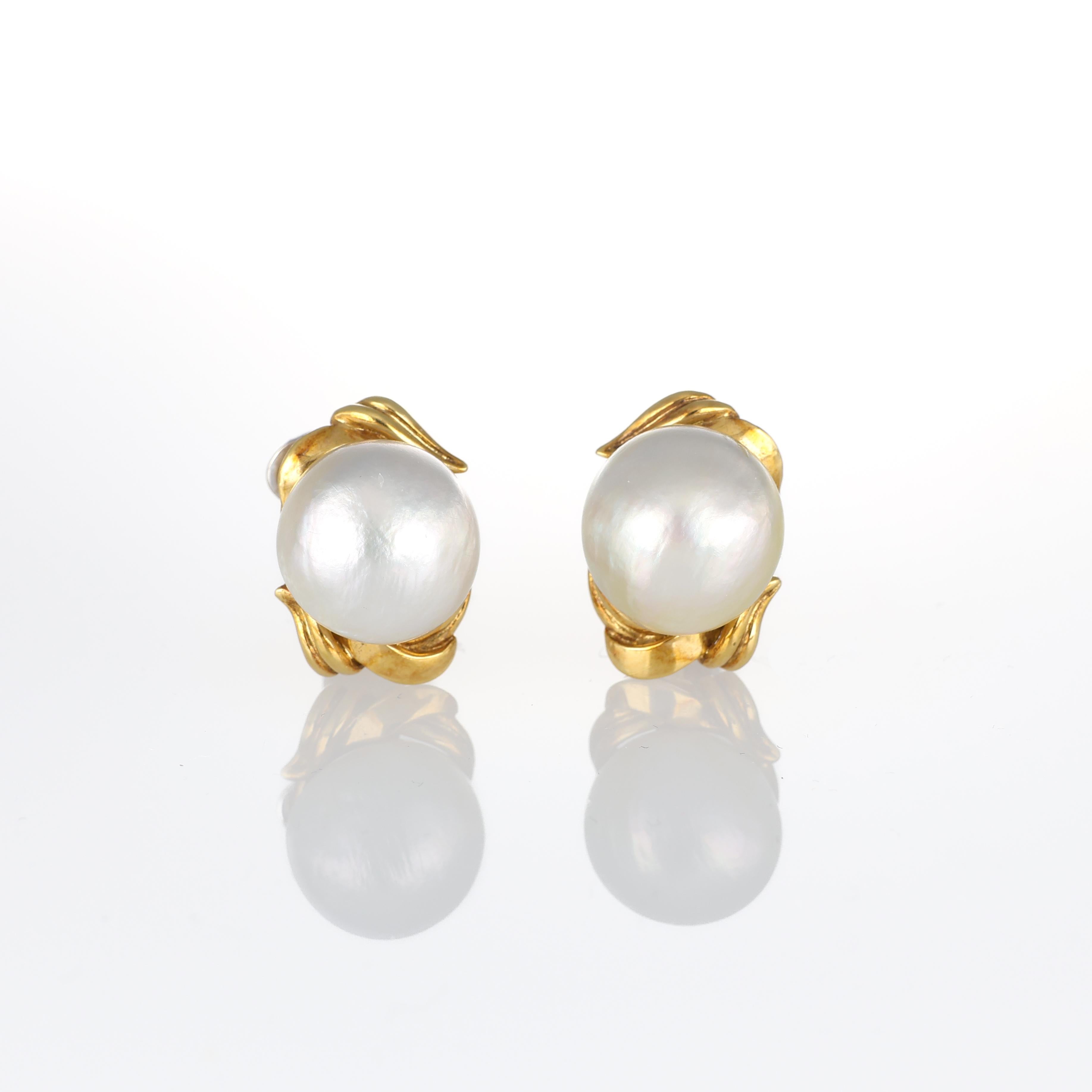 A timeless expression of elegance, these pearl stud earrings are crafted in 18K yellow gold. Each earring features a luminous natural pearl set in an organic gold frame, creating a refined and sophisticated look. The soft glow of the pearls