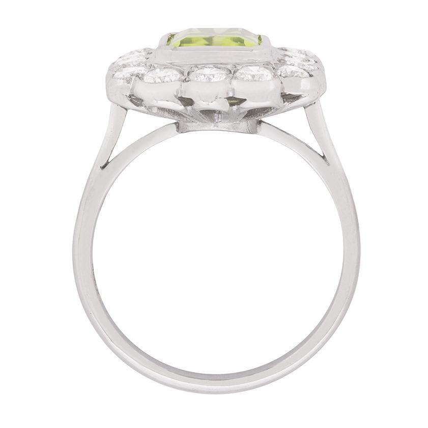 
This lovely ring centres a 2.60 carat emerald cut peridot embellished at its outer edge by a single row of well-matched round brilliant cut diamonds weighing 1.40 carats, all set within a pretty 18 carat white gold openwork gallery.

Gemstone: