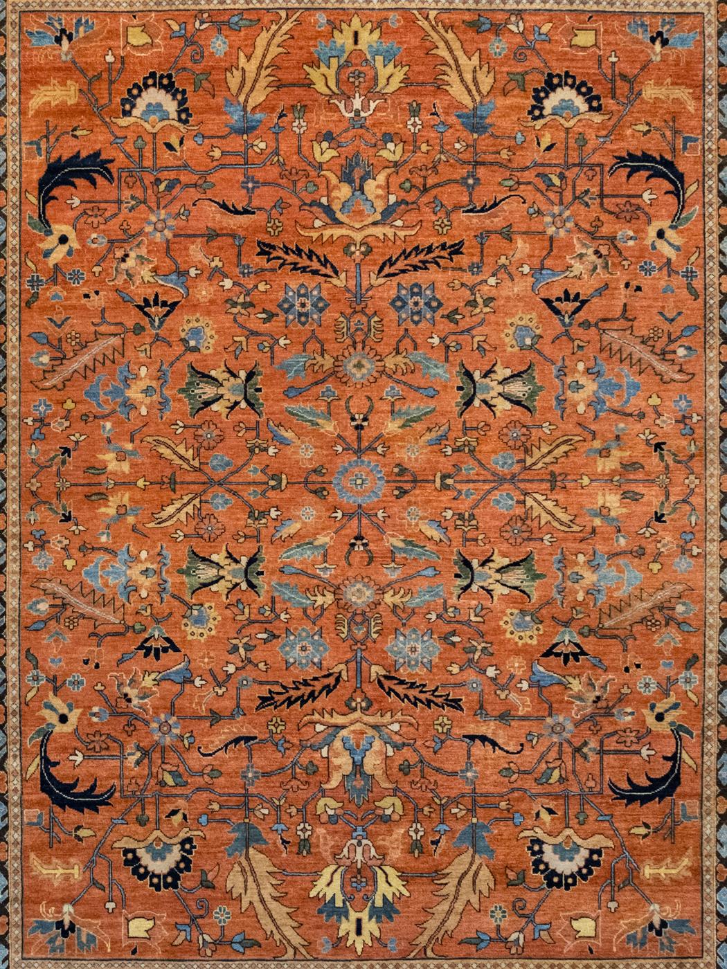 Utilizing a classic symmetrical design, this modern Persian Serapi carpet measures 7’10”x9’10” and is detailed in shades of orange, indigo, gold, cream, and black wool. Blooming from a small floral medallion, tribal-inspired flower bulbs,