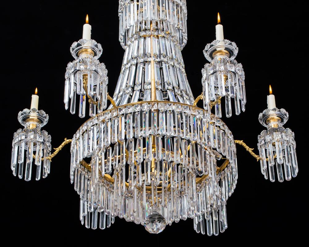 A fine Regency chandelier of Classic tent and waterfall design with drop hung corona the main ring issuing six scroll arms supporting drop hung drip pans and candle nozzles with fan cut scallops the waterfall with four concentric rings terminating