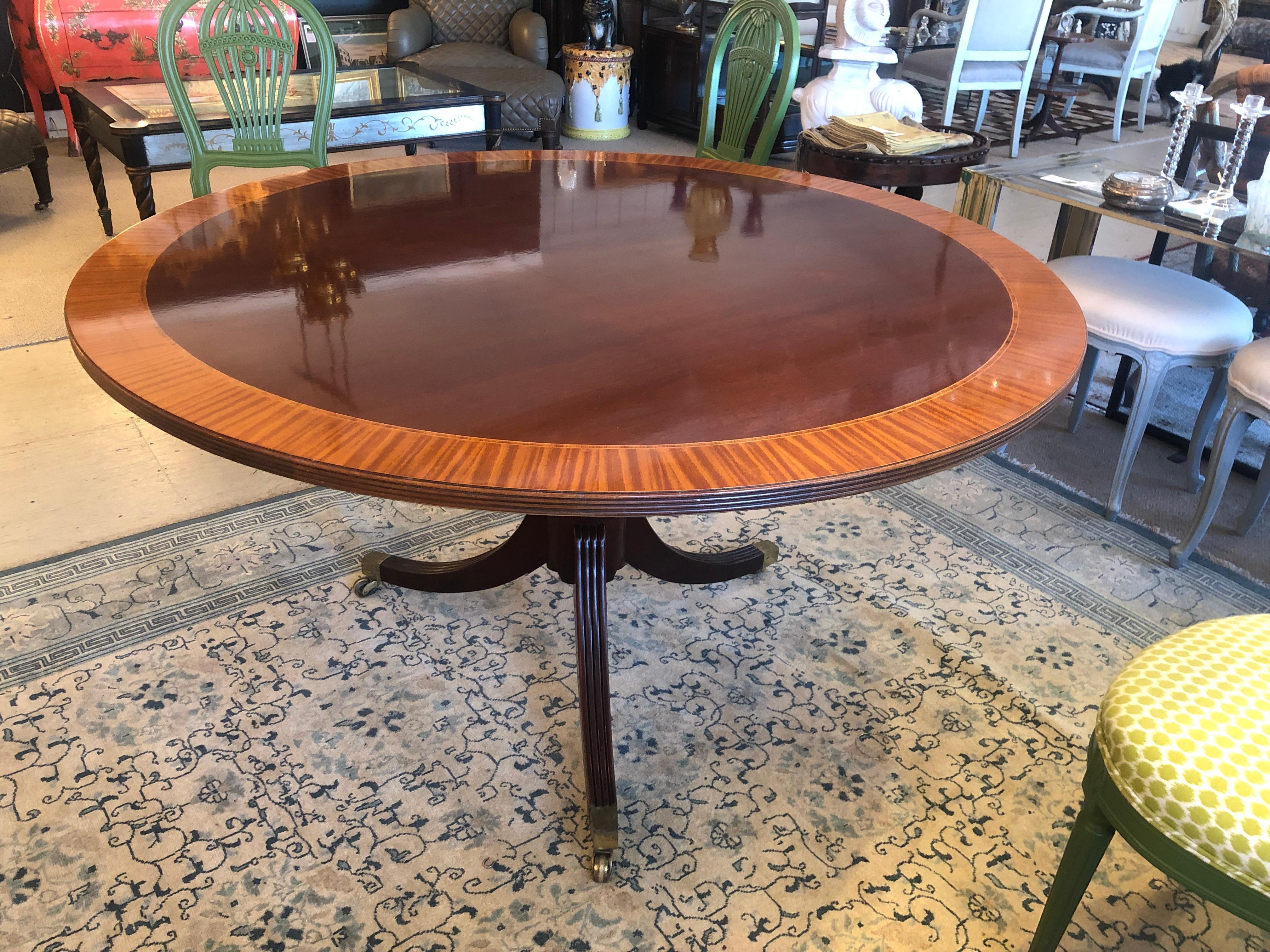 Classic Regency style banded mahogany and satinwood round table having carved pedestal and elegant splayed tripod legs capped with brass tips and casters. The color is especially rich and inlay around the periphery makes a beautiful contrast.