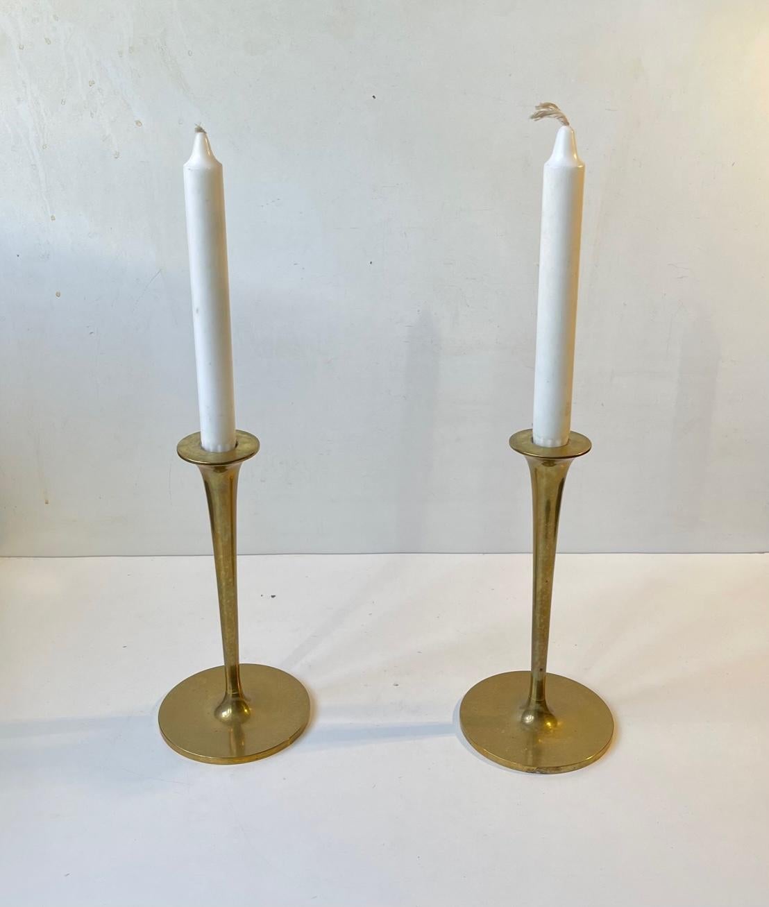 A pair of trumpet shaped brass candlesticks designed and manufactured in Scandinavia during the 1960s. The candlesticks are in a heavy quality and are to be fitted with regular sixed candles. They have not been polished recently and display patina.