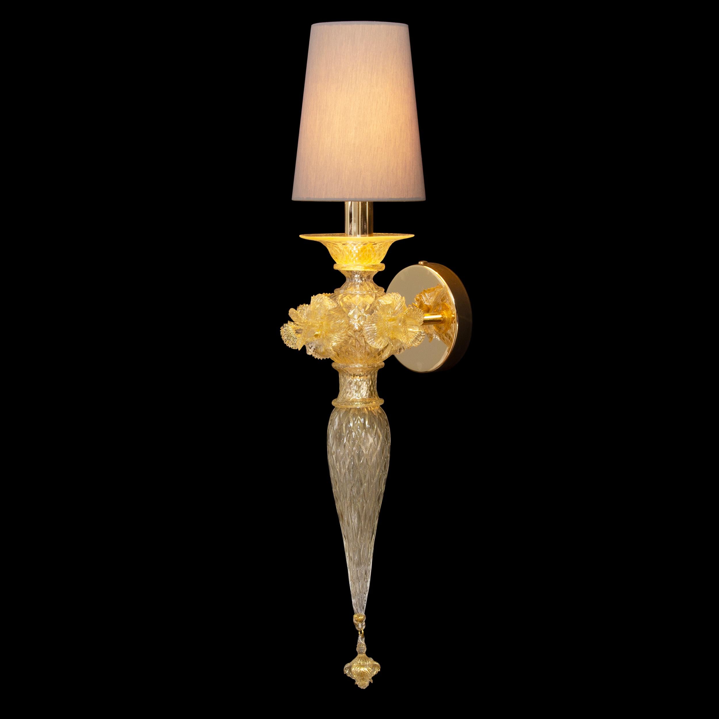 Single sconce 1 light in clear and gold Murano glass. Details with flowers by Multiforme.
To manufacture this sconce there has been used a “balloton” texture (a grid-like surface) while some flowers decorate the central part of the structure. The