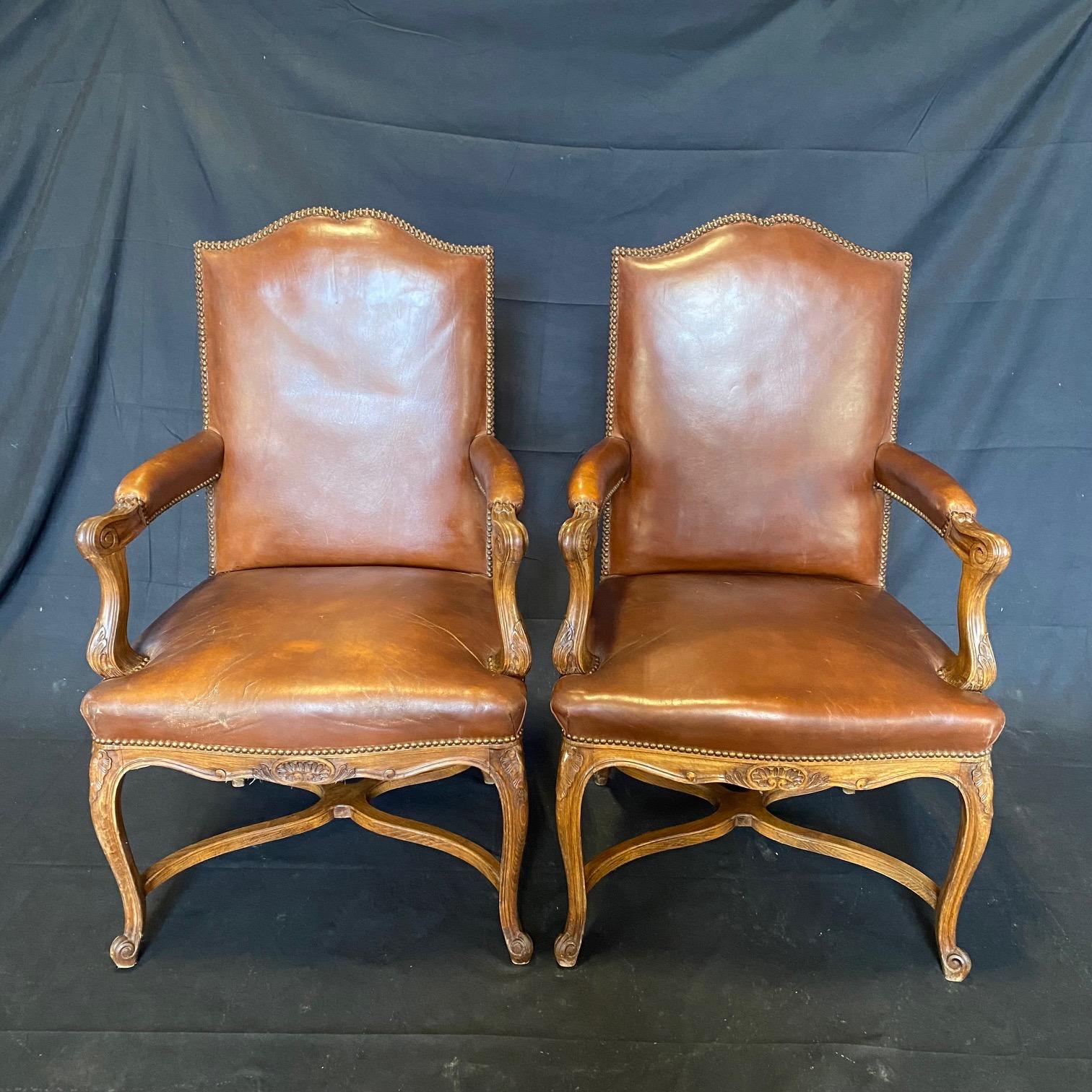 A set of three Louis XVI style vintage French carved wood and leather upholstered armchairs from the early 20th century featuring elegantly shaped backs, flanked within prominent shoulders that flow gently down onto the arms which terminate into