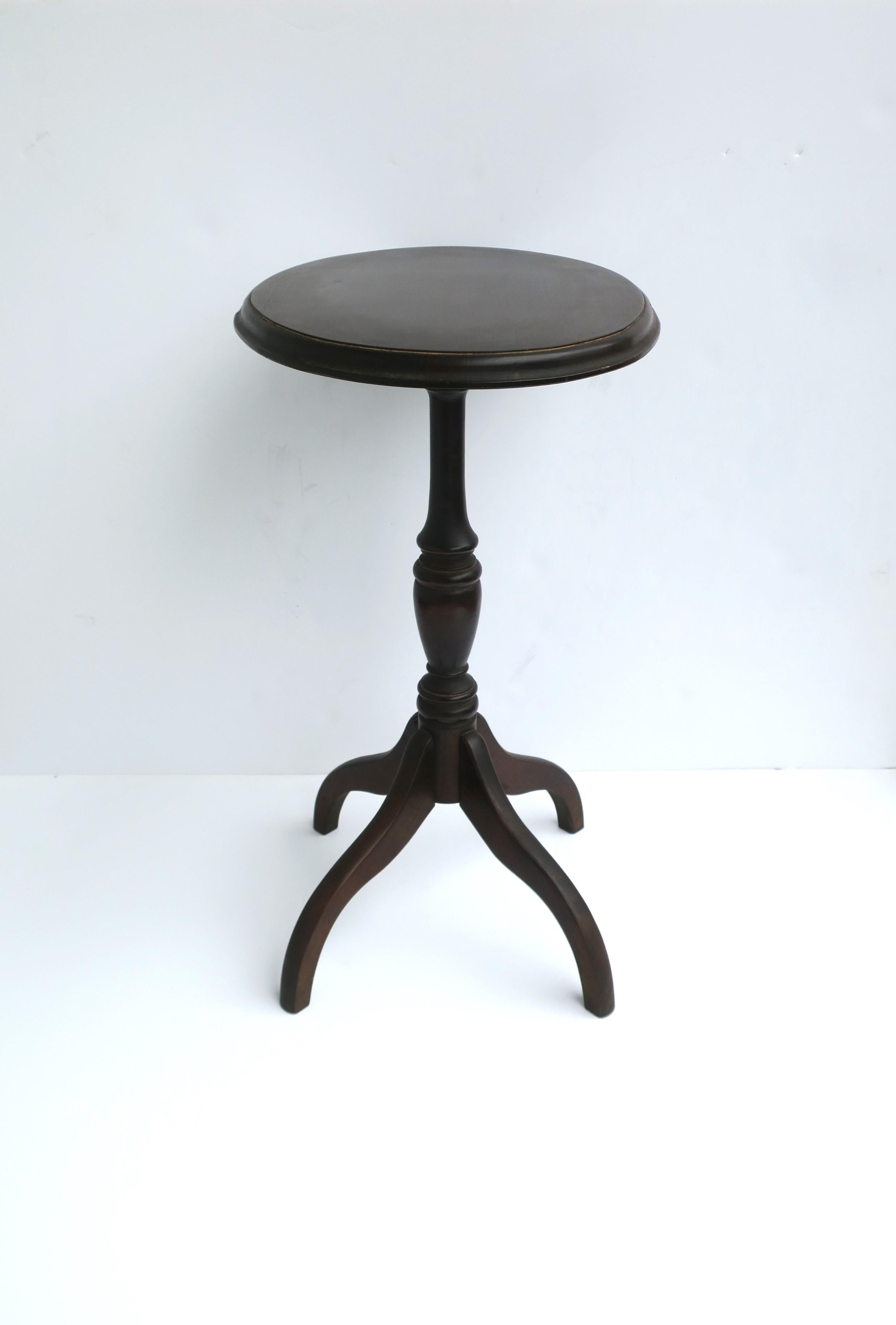 A Mahagany wood oval top side or drinks table, circa mid-20th century, USA. Table is also known as a 'candle stand table' referring to antique versions of tables' style/design. Table has a wood veneered oval top, turned neck and 'spider' legs. Piece