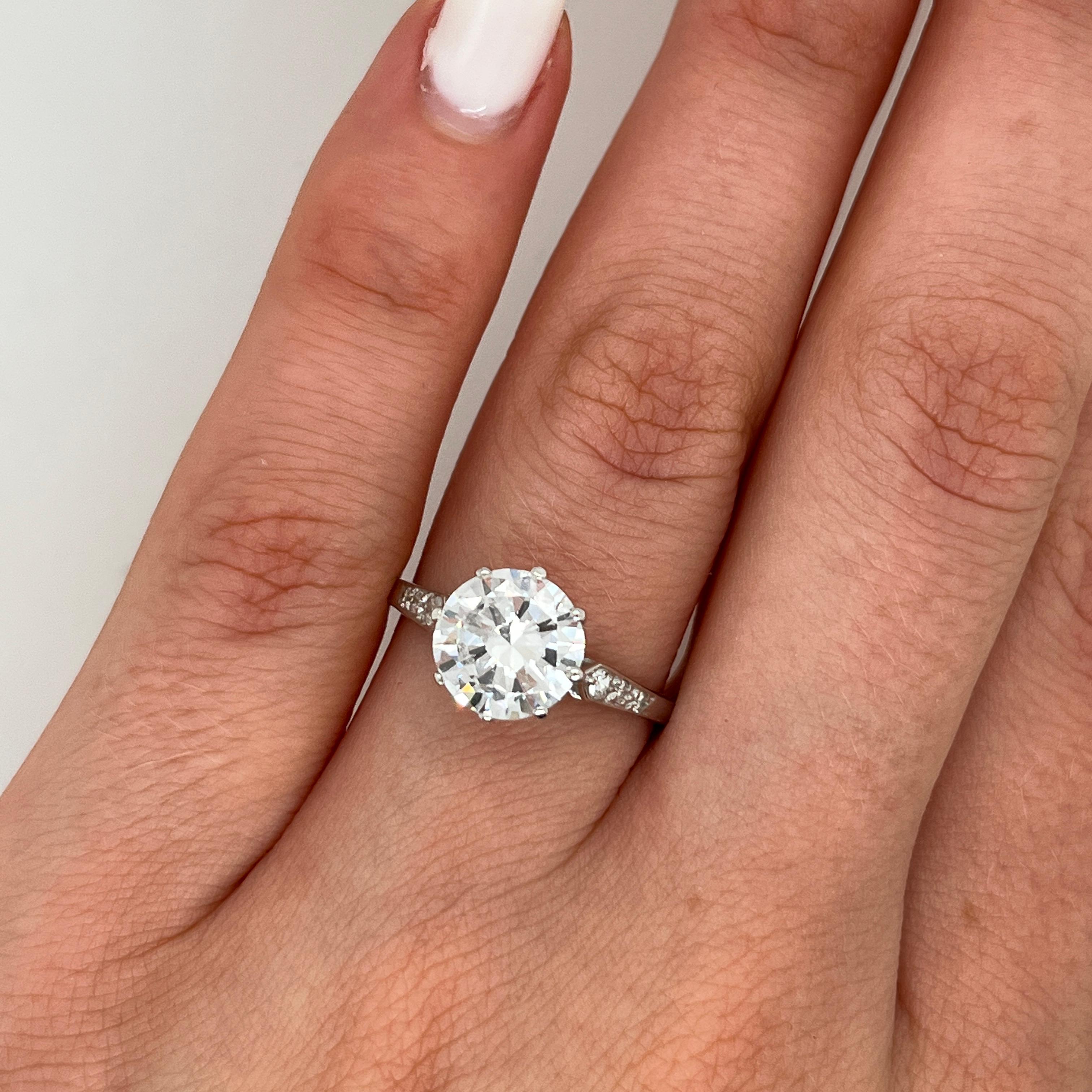 Cette élégante bague de fiançailles est ornée d'un diamant rond de taille brillant de 1,98ct, 
solidement niché dans un anneau de conception classique avec de petits diamants sur les épaules. 
Réalisée en platine, la simplicité intemporelle de cette