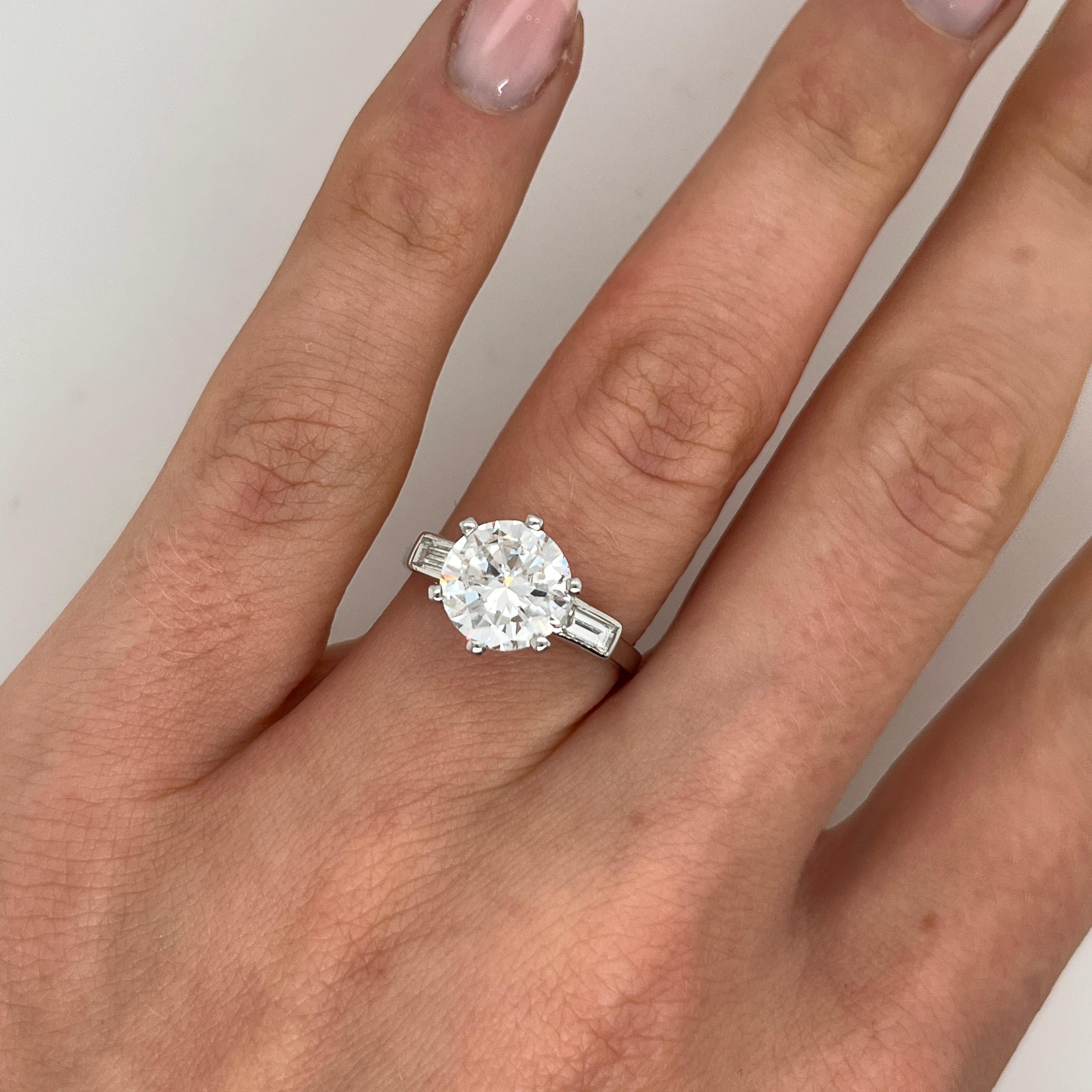 This elegant engagement ring features a 2.32ct round brilliant-cut diamond, securely nestled in a classic design band 
with 2 matching baguette diamonds on sides. Crafted from platinum, the timeless simplicity of this piece highlights the diamond's