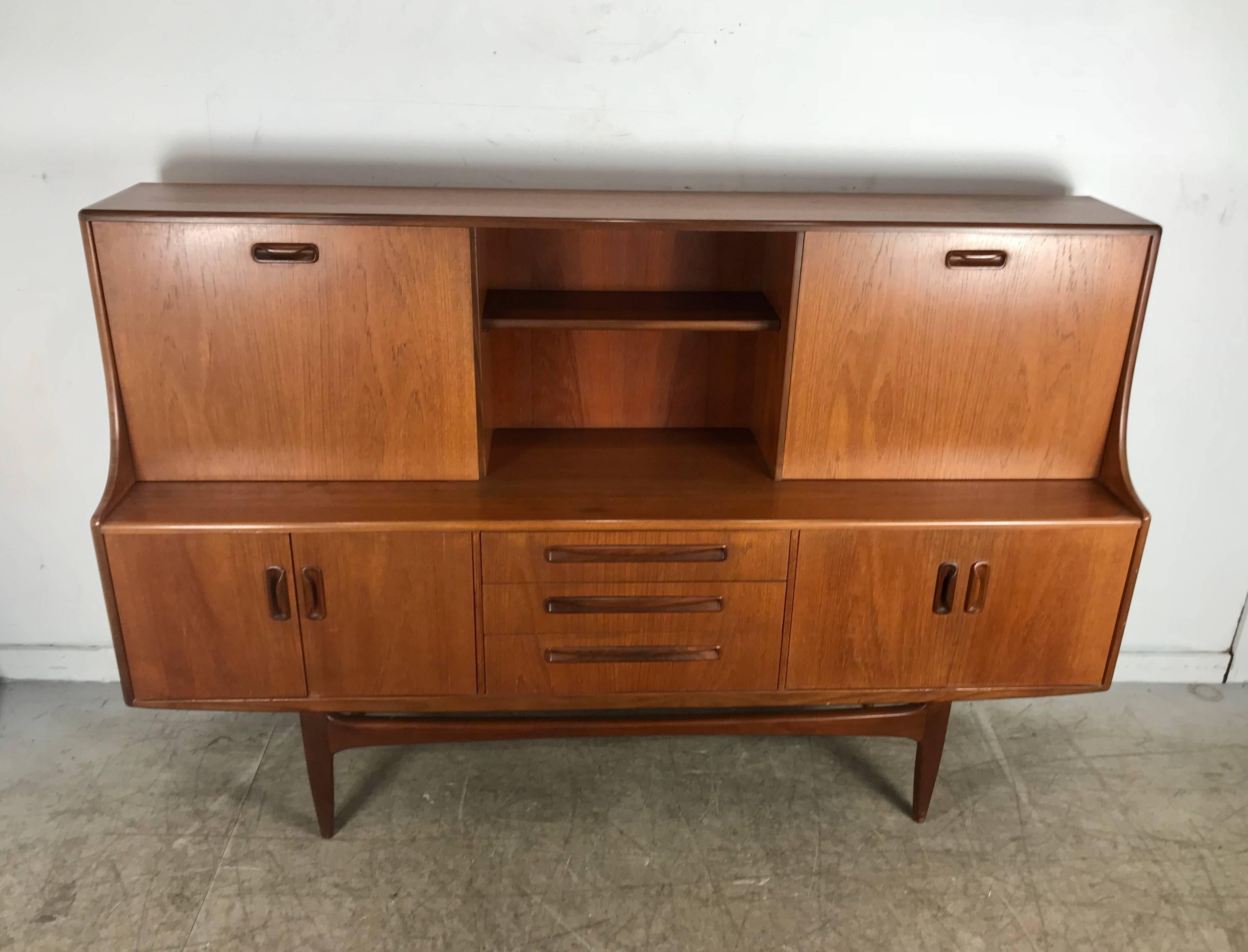 Classic teak Danish modern Credenza, cabinet by Ib-Kofod Larsen. Top featuring sliding door, drop down desk. Bar surface,Bottom left and right doors ,three drawers,top with flatware compartments, Superior quality and construction, hand delivery