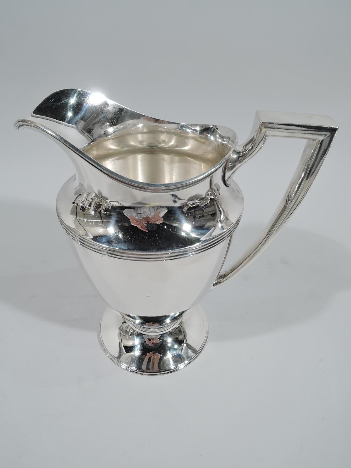 Classic sterling silver water pitcher. Made by Tiffany & Co. in New York. Curved and tapering body, raised and stepped foot, scrolled bracket handle, and helmet mouth. Reeding. Fully marked including pattern no. 18181, director’s letter M (1947-56),