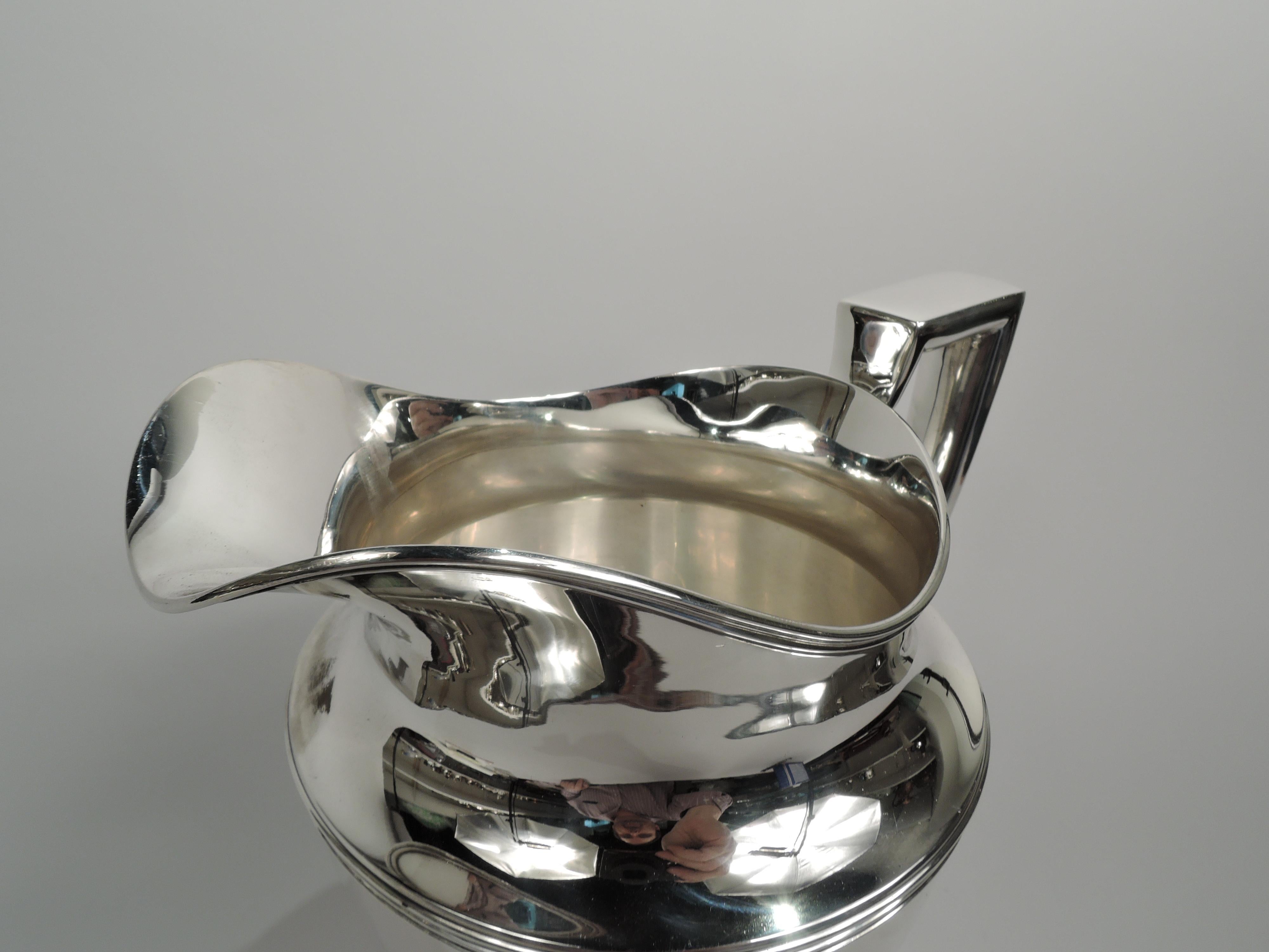 Classic sterling silver water pitcher. Made by Tiffany & Co. in New York, ca 1911. Curved and tapering body, raised foot, scrolled bracket handle, and helmet mouth. Reeding. Fully marked including maker’s stamp, pattern no. 18181 (first produced in