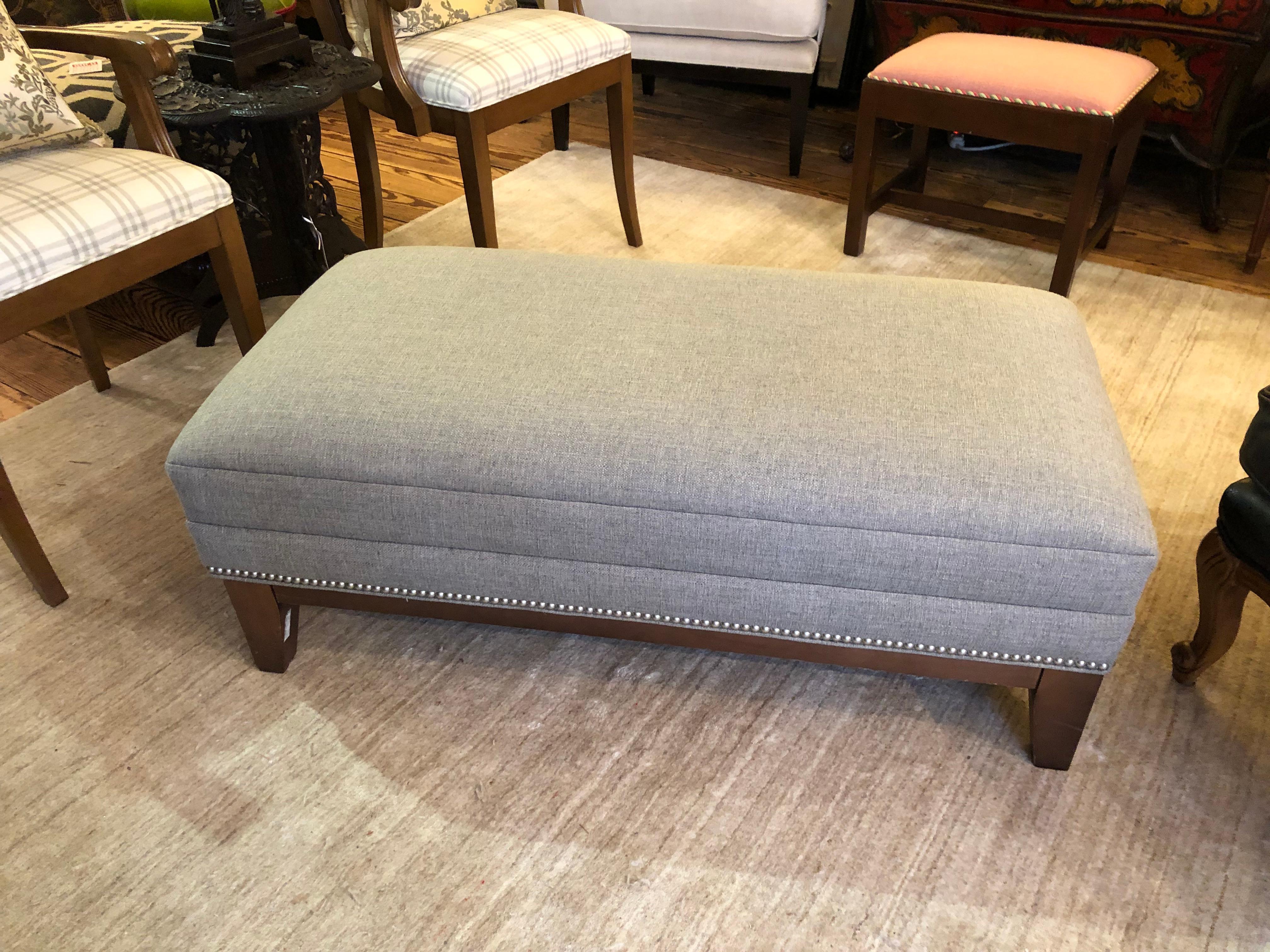 A versatile and handsome greyish beige (greige) upholstered rectangular ottoman finished with nailheads. Great for extra seating, a place to put your feet, or used as a coffee table. Good at the end of a bed too. Purchased at ABC Carpet in NY about