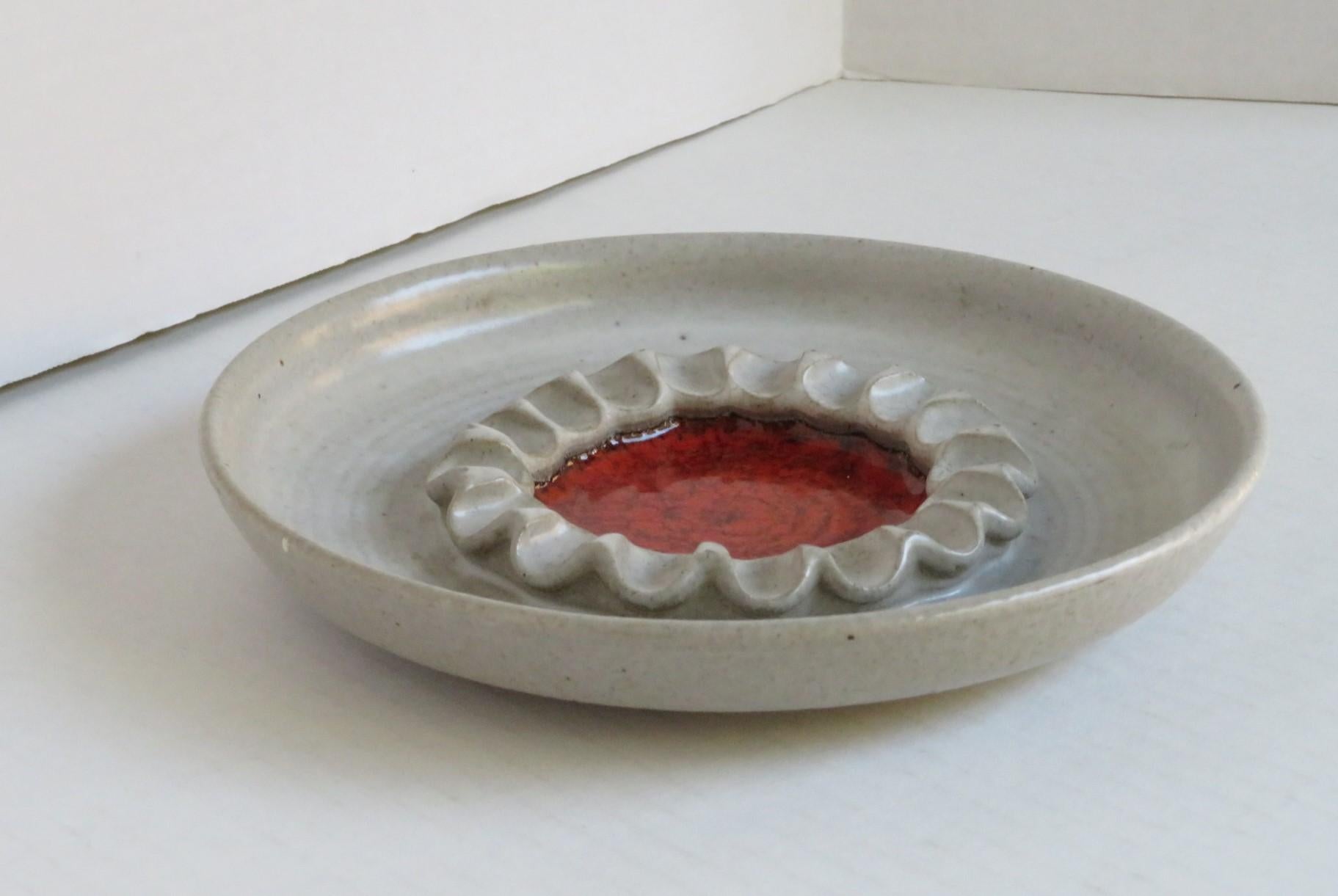 An enticing pottery design by Victoria Littlejohn, hand thrown Dish with a wonderful neutral oatmeal color glaze with a central red orange crystalline thick glaze surrounded by a crimped wall. Possibly designed as an ashtray considering the time