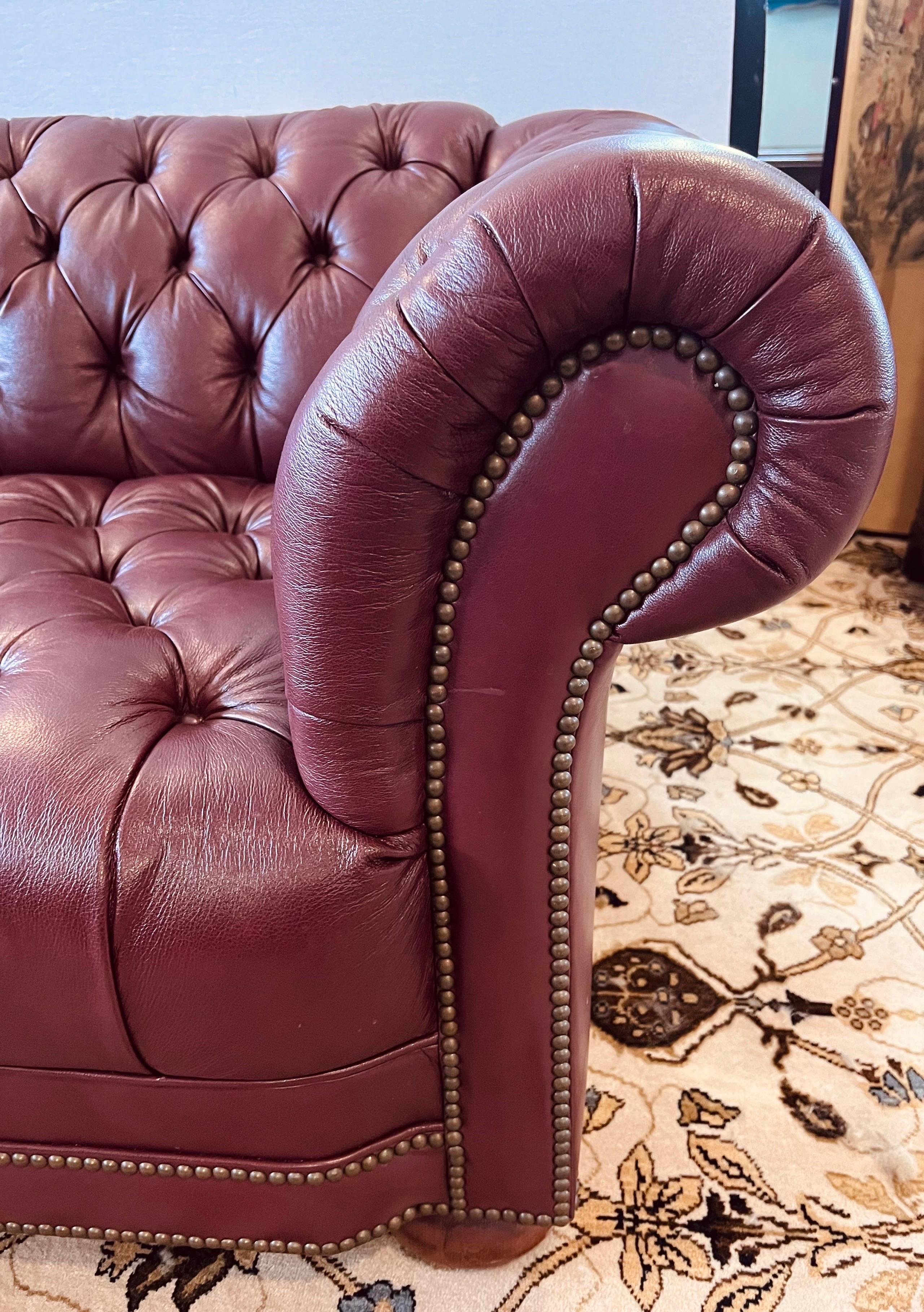 Handsome, handcrafted in the USA, burgundy button tufted leather chesterfield sofa  with scrolled arms and finished with brass nailhead trim and raised on mahogany bun feet. Button tufted on the seat, back and arms.
We can help with shipping and