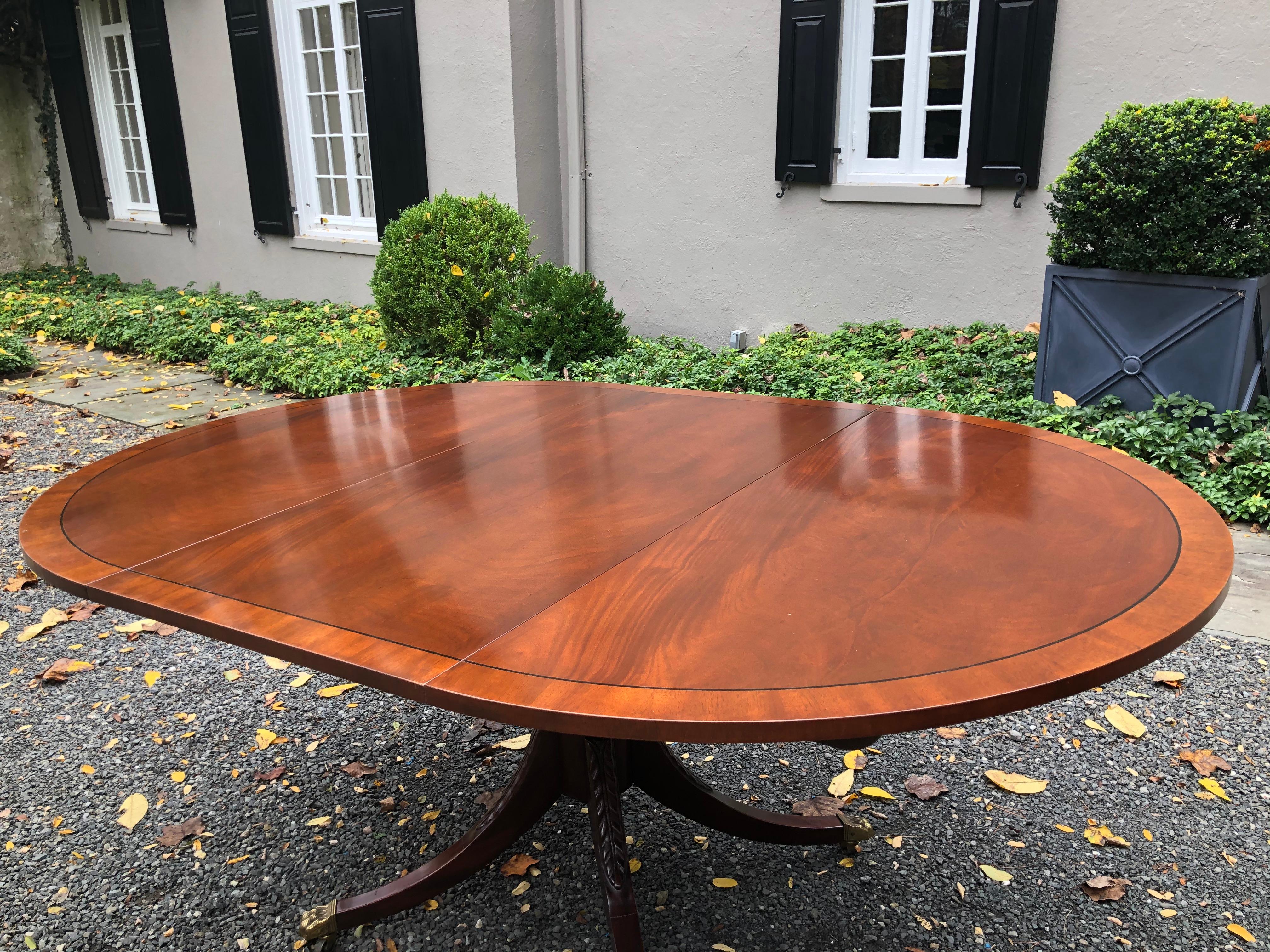 Vintage mahogany Sheraton style dining table by Baker. Part of the Historic Charleston Collection, this table has banding and string inlay around the perimeter. There is carving on the pedestal and legs and brass casters in the lion’s paw feet. The