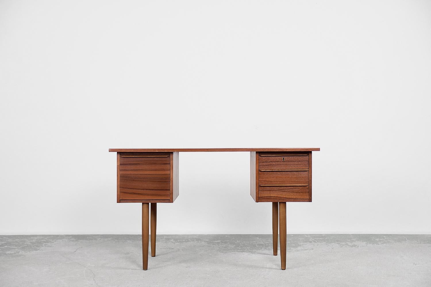 This classic desk was made in Sweden during the 1960s. It has been finished in teak wood in a warm shade of brown, with visible grain details. The desk has three smaller, flat drawers locked with a key on one side and one deep drawer on the other