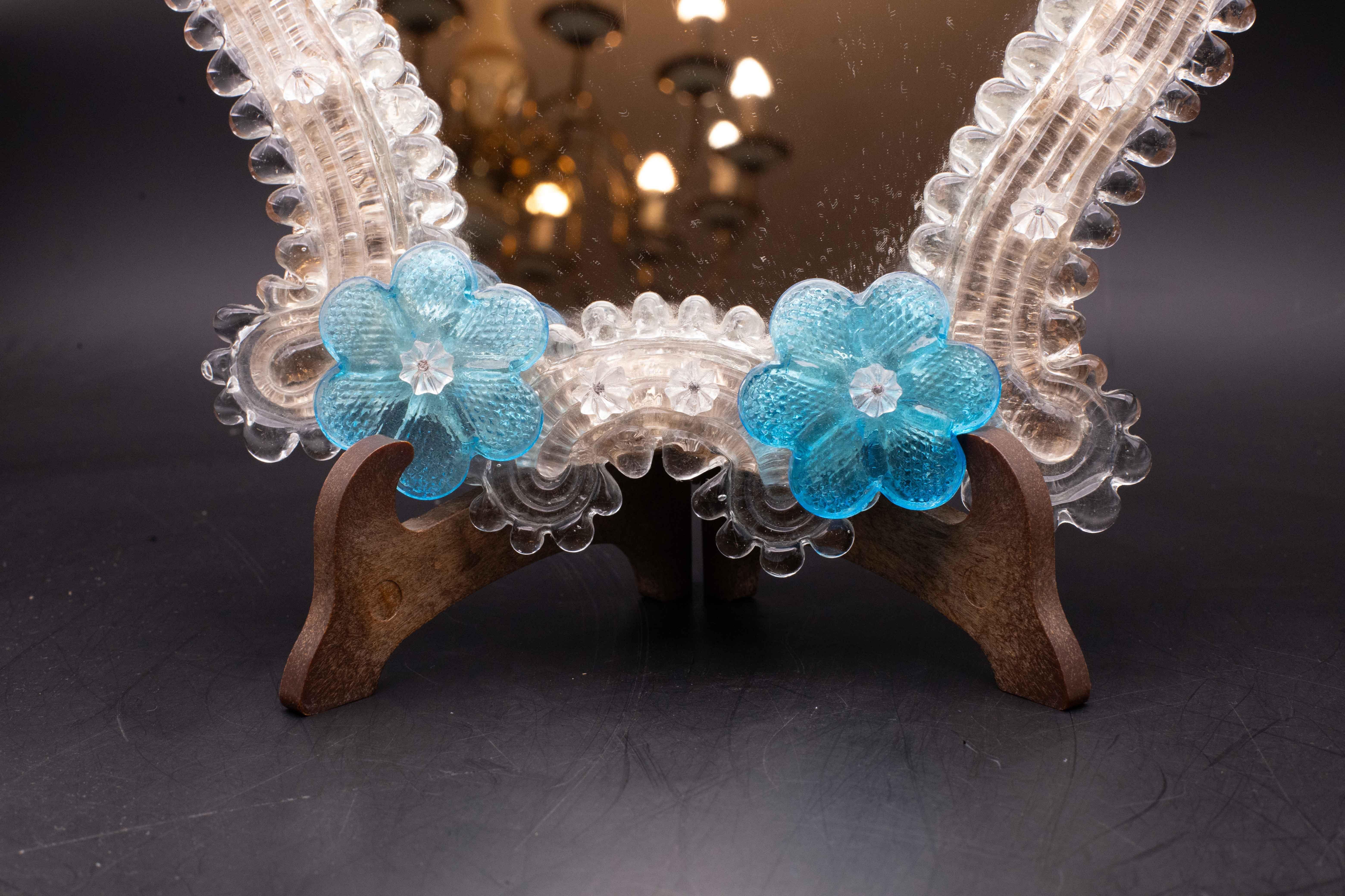 Specchio classico veneziano con lavorazione tipica di Murano.

Lo specchio è decorato con 4 tipici fiori azzurri.

Eccellenti condizioni vintage.

Altezza 25 centimetri, larghezza 23 centimetri.