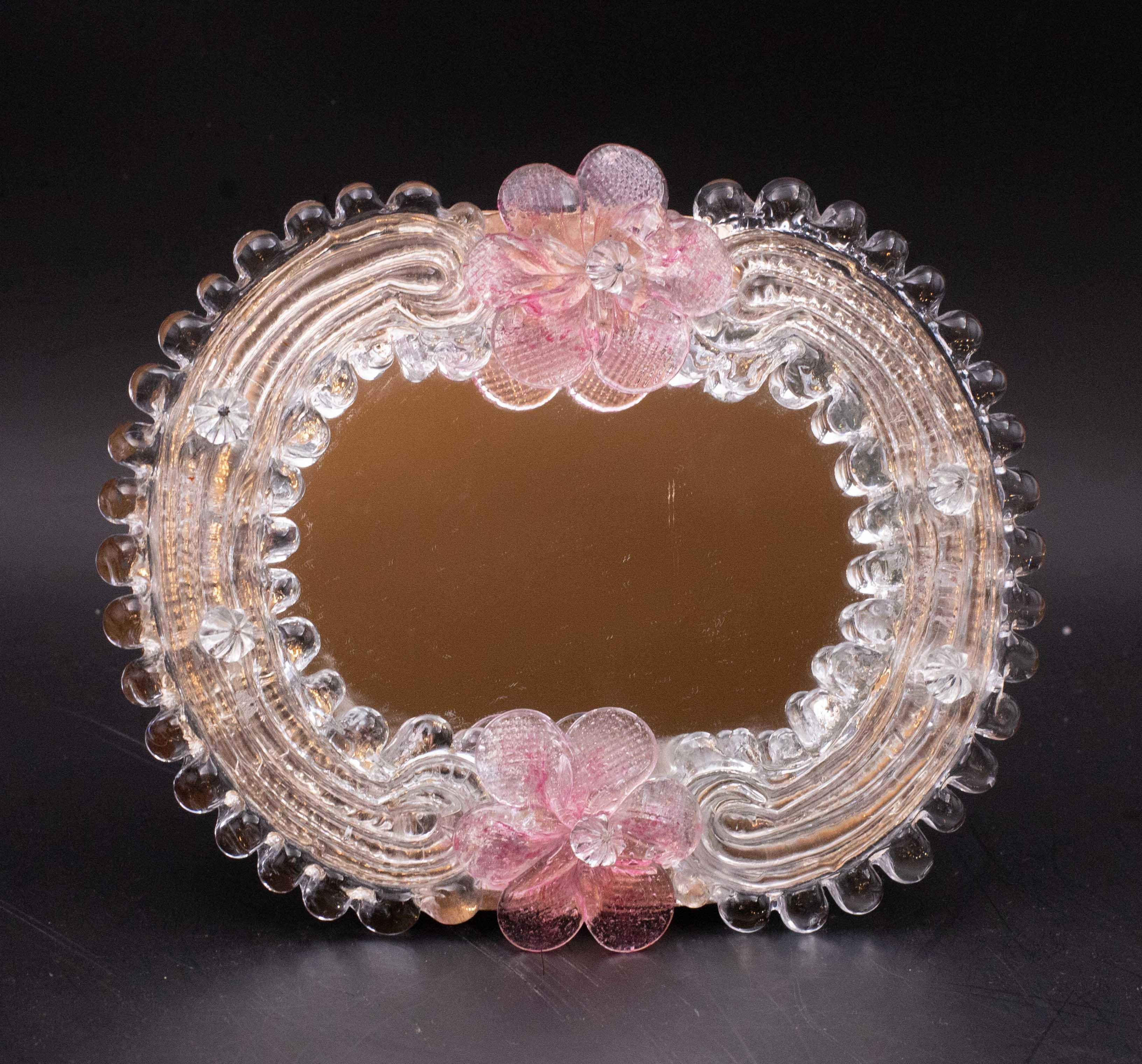 Specchio classico veneziano con lavorazione tipica di Murano.

Lo specchio è decorato con 2 tipici fiori rosa chiaro.

Eccellenti condizioni vintage.

Altezza 15 centimetri, larghezza 17,5 centimetri.