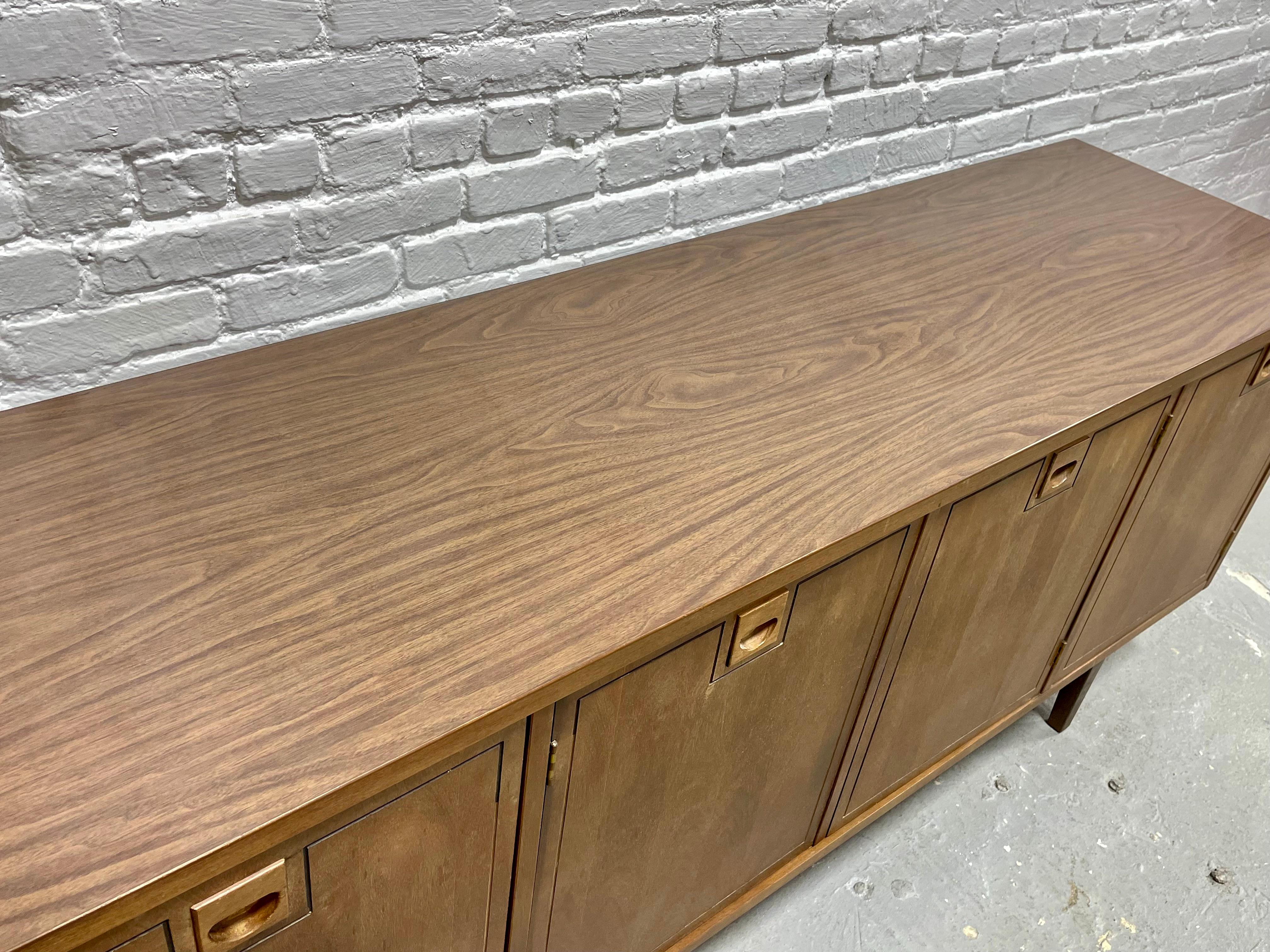Simple + Classic Mid Century Modern Walnut Credenza / Media Stand designed by Stanley Furniture Co., c. 1960's. This classic credenza features a simple front panel design behind which is a perfect layout for a media stand - generous shelving for