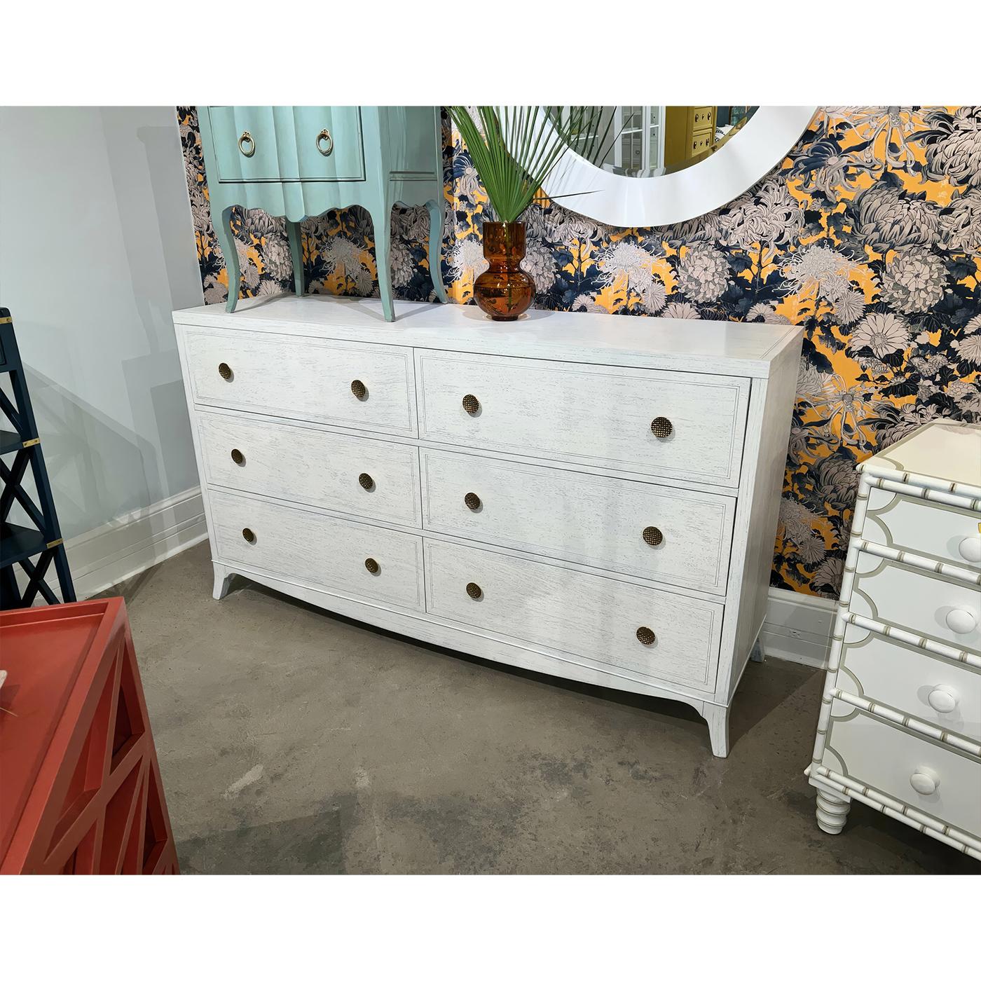 The crisp white finish creates a bright, clean canvas that highlights the dresser's architectural elements, while decorative basket weave brass knobs add warmth and sophistication to each of the six soft close drawers. Traditional English