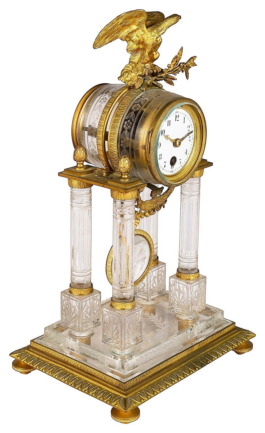 A classical crystal 19th Century French Empire style portico mantle clock, with a gilded ormolu Eagle, white enamel clock face and four column supports engraved decoration and a plinth base.
 
Batch 73 62104. DZZZN