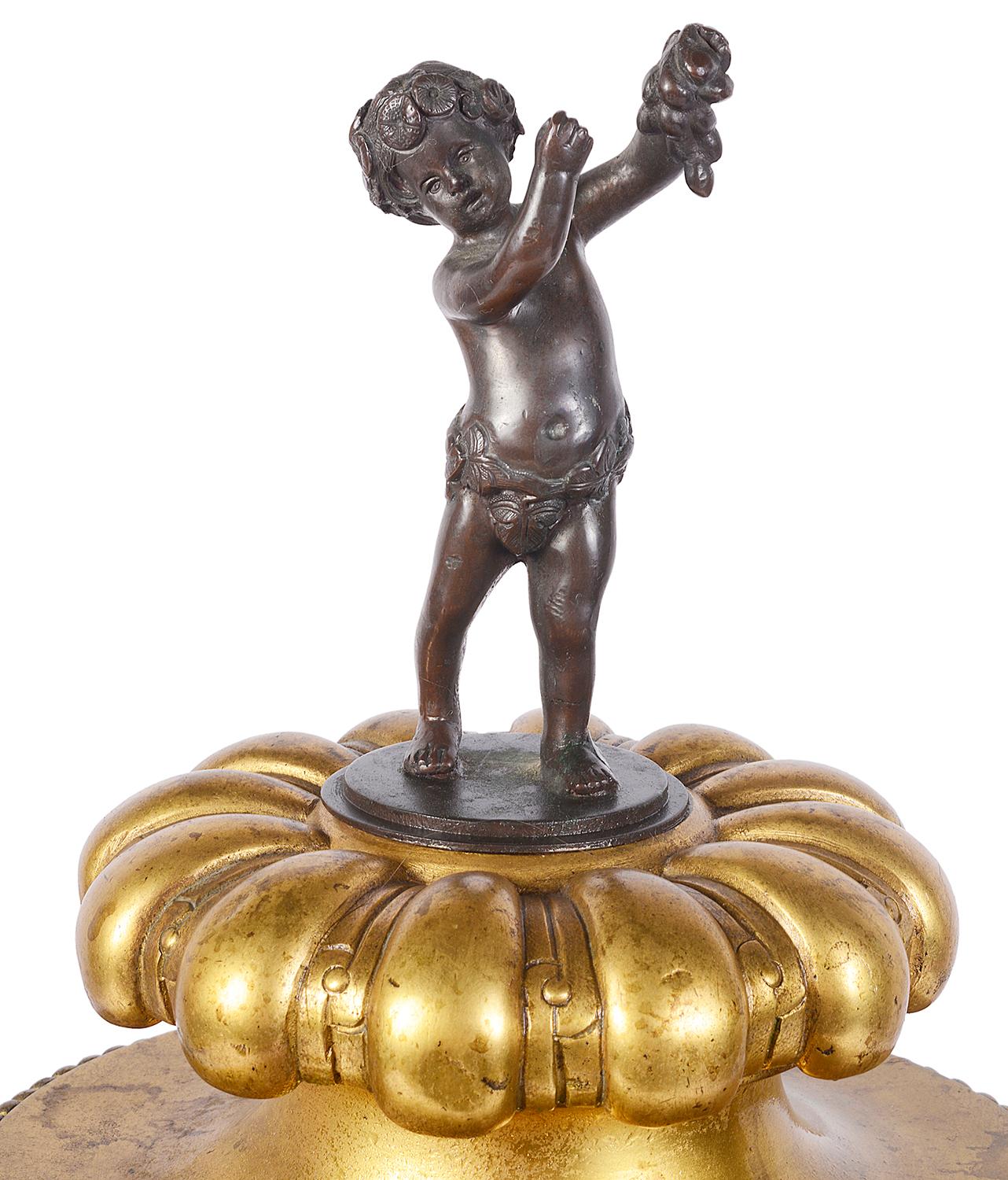 A good quality 19th century Italian gilded ormolu and bronze lidded urn, having a young boy holding fruit as a finial to the lid, foliate and acorn relief decoration, a boars head handle to either side, Greek key pattern and further oak leaf and