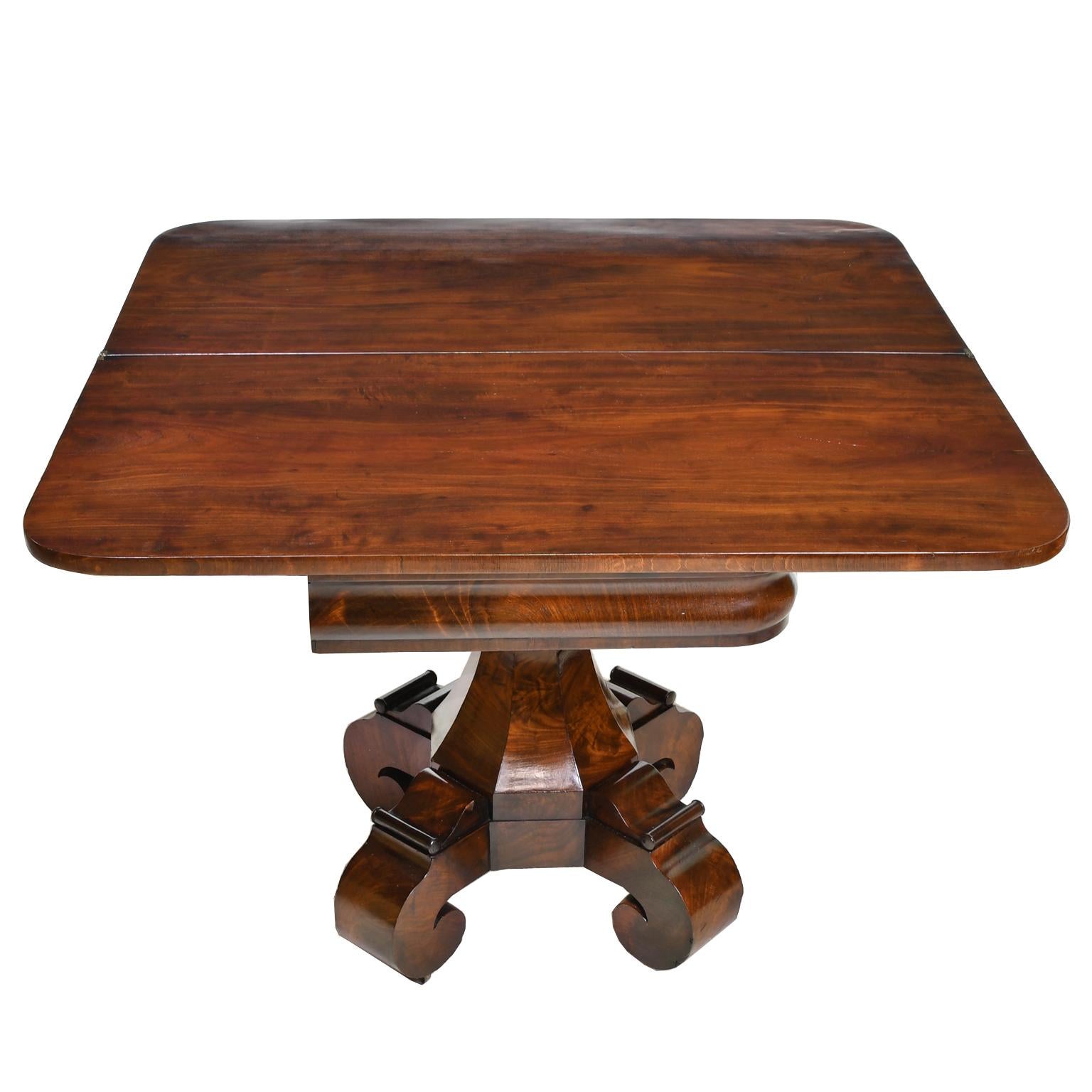 An exquisite classical American empire card or games table in fine West Indies/ Cuban mahogany in the Grecian-style with octagonal support column resting on quatre-form pedestal base with scrolled feet. Th hinged rectangular top turns & opens to a