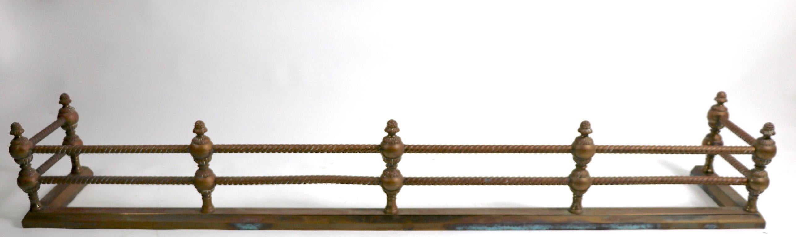 Brass fender, with twisted rail horizontal rods held by classical styled vertical supports. Total H 10 inch, top rail H 8 inches. Finish shows patina and wear, normal and consistent with age. Solid brass construction.