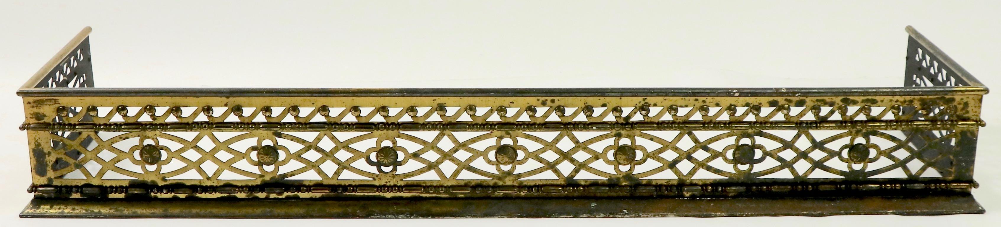 Classic brass fender having  a reticulated frame work with quatrefoil, wave and egg and dart pattern designs. The fender is free of structural damage, bends, breaks or repairs, the finish shows significant cosmetic wear, normal and consistent with