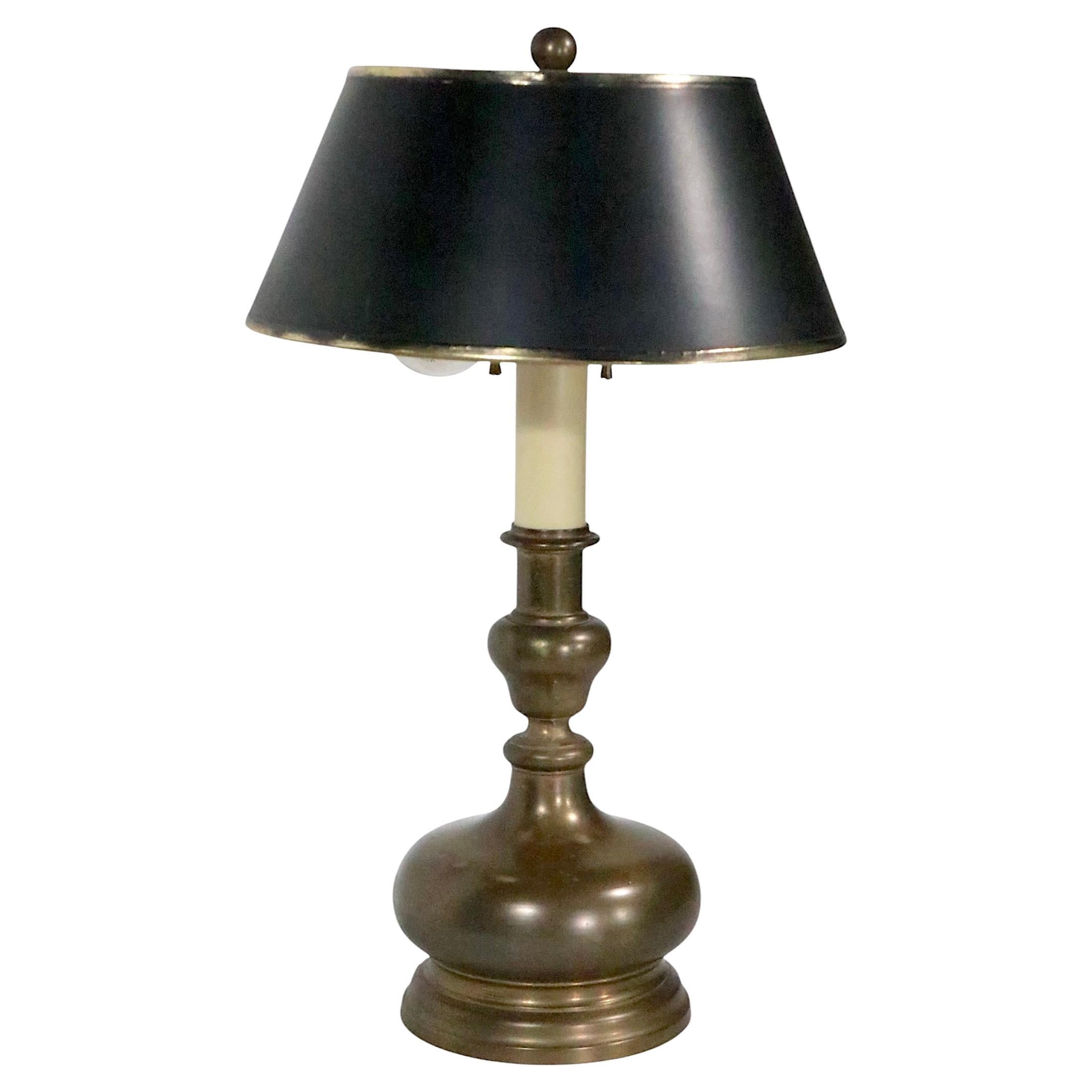 Brass table lamp having a bulbous form base, with a candlestick column that supports two pull chain sockets. The lamp includes it's original paper shade which shows minor wear, normal and consistent with age. 
 Lamp Base:
 Dia. 7