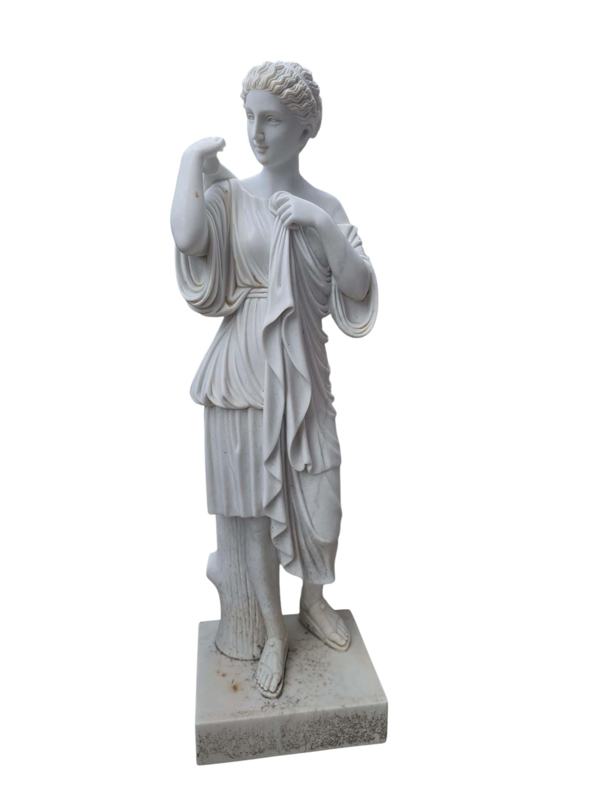 Refinada escultura de mármol tallada a mano que representa a Diana, la antigua diosa grecorromana de la caza y la luna. Fabricada en Italia durante el siglo XX con fino mármol blanco de Carrara, la figura está representada en una pose clásica, con