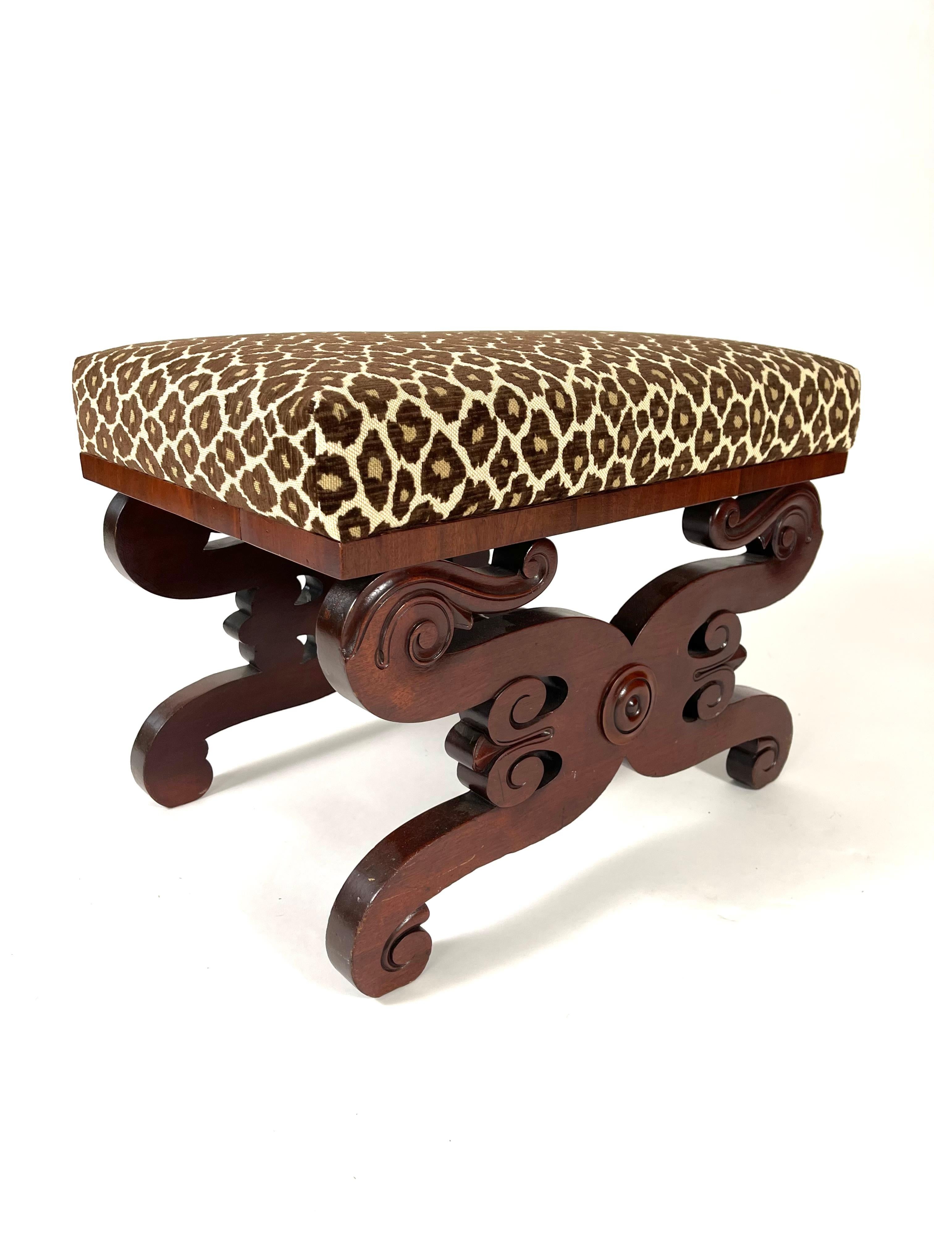 A Classical carved mahogany footstool, or ottoman, the top newly upholstered in leopard print velvet fabric over scrolled supports joined by a vase and ring-turned stretcher, Boston, circa 1820.  Beautifully made and very solid, this stool may serve