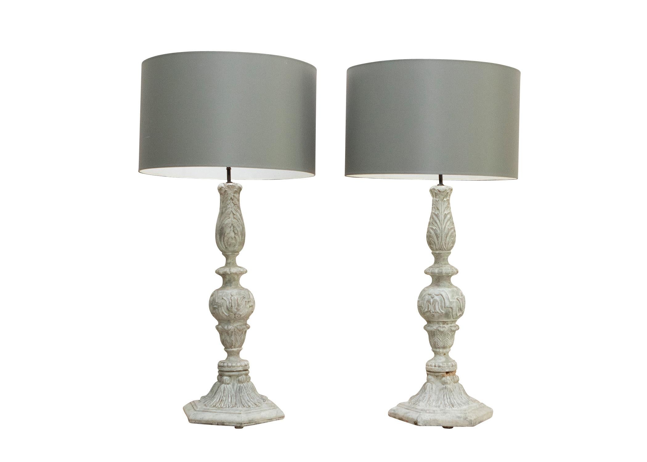 Oversized carved wooden finial lamps with classical decoration and grey drum shades. Painted to look like stone finials with tassel decorated bases and foliate design. 30 inches in height without shades, 42.5 inches with grey drum shades.