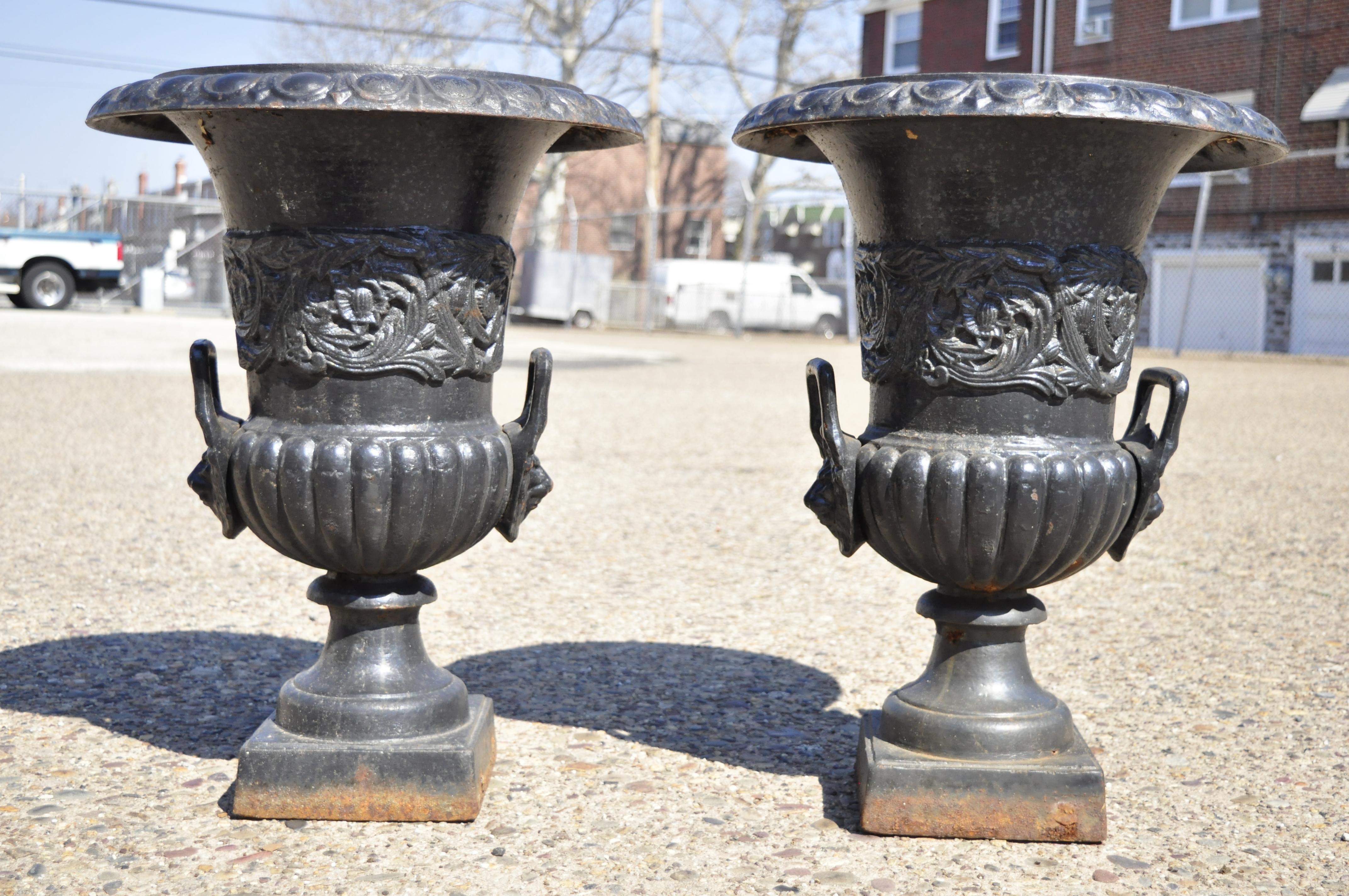 Vintage classical cast iron figural urn garden planter pots with lions and foliate - a pair. Item features lion form handles, leafy scrollwork, heavy cast iron construction. Circa mid 20th century. Measurements: 24