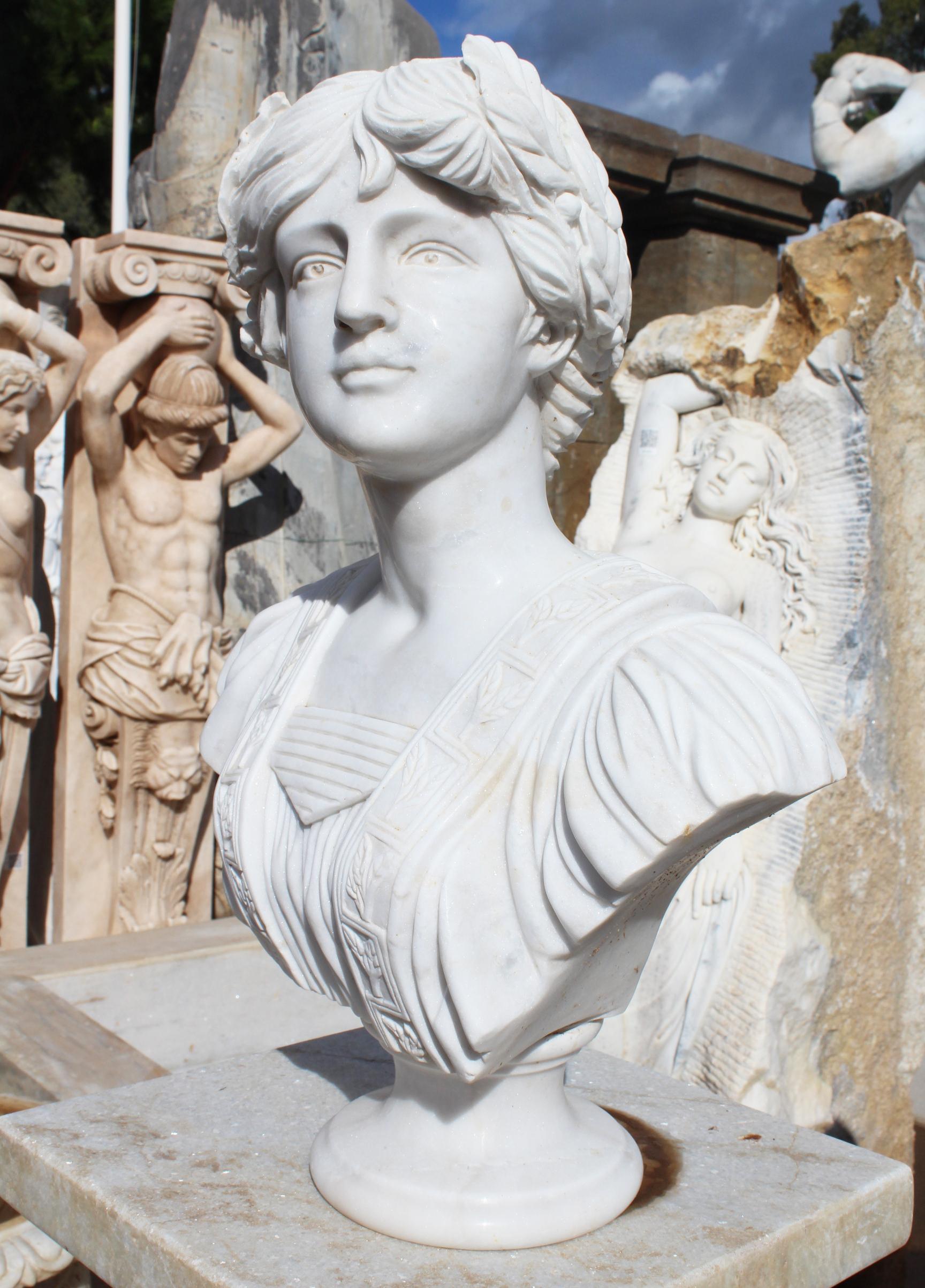 Classical hand carved white marble bust of a woman wearing Greek period dress and a laurel wreath.
 