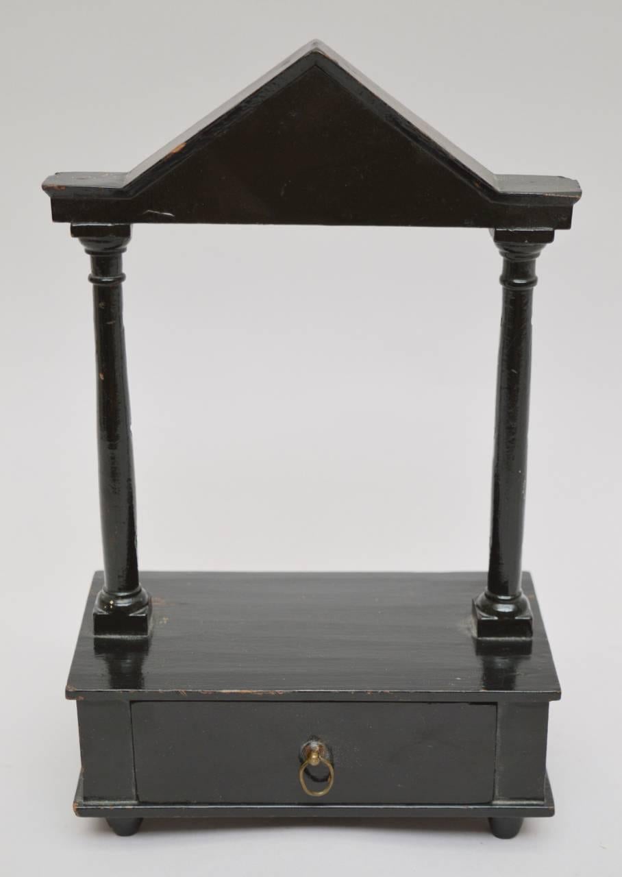 An elegant pocket watch Stand having one drawer and a classical pediment with columns. The watch is meant to be placed on the hook at the back of the pediment to allow it to hang between the columns.