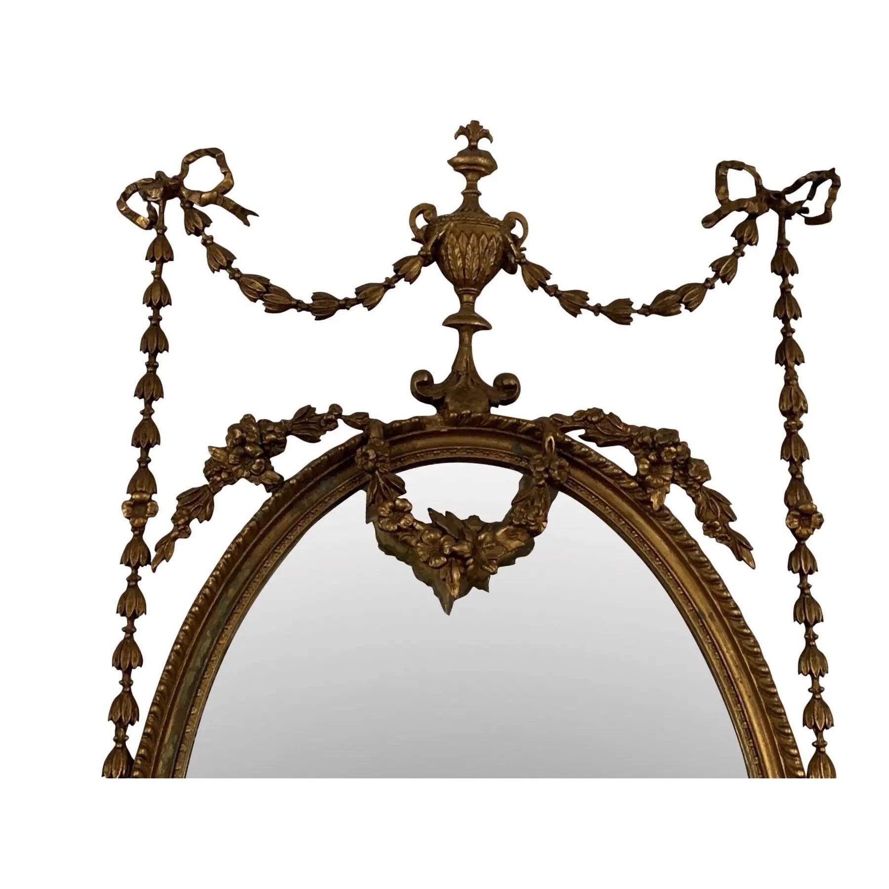 A Classical oval gilt wood and gesso mirror with original beveled glass. The oval frame is carved with a floral wreath and surmounted with an urn finial and trailing flowers. Below are scrolled acanthus leaves and more trailing flowers. Circa 1880.