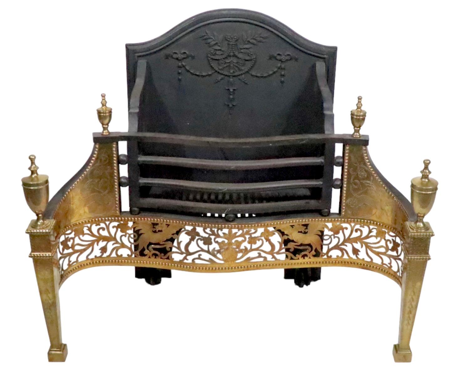 Impressive English  fireplace coal grate insert having a cast iron frame with decorative foliate elements, fronted by a bright solid brass structure with a hand etched surface, showing fantastical winged animals  etc,  and tapering fluted column