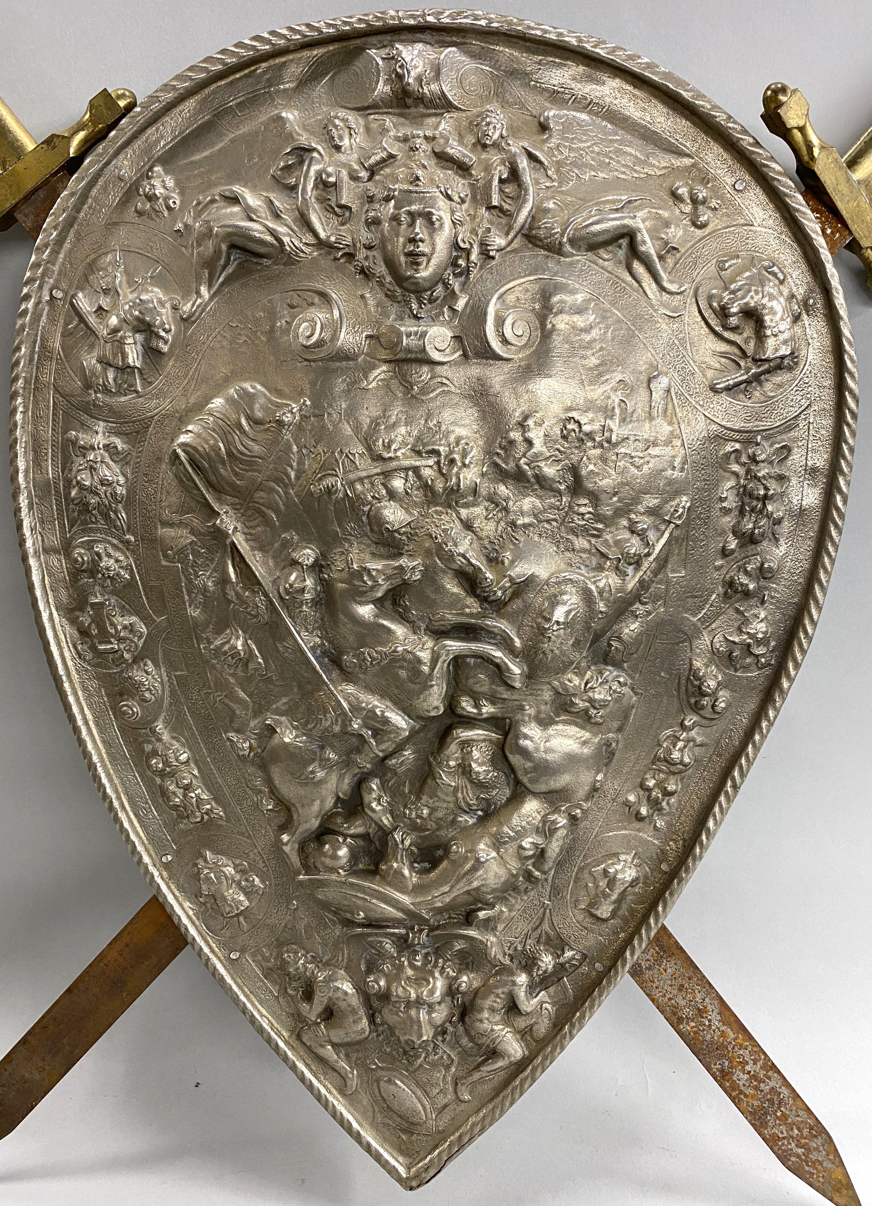 A fine pair of Classical Revival ceremonial swords with brassed handles, attached to a pressed steel shield with nickel plating featuring classical, angelic and military figures, some on horseback, and ram’s head accented with scrollwork and foliate