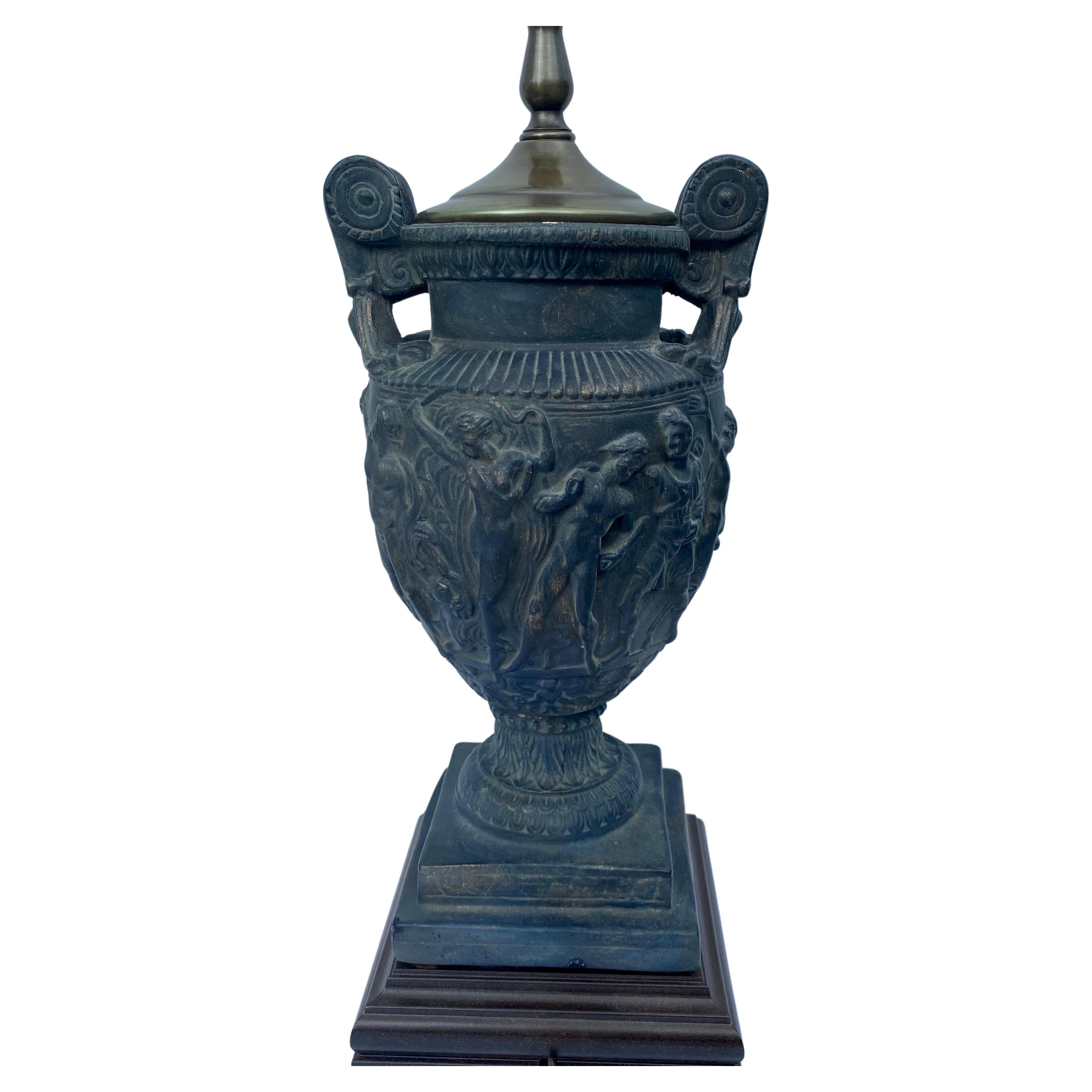 Lampe de table en forme d'urne à poignée classique montée sur un socle en bois carré. Cette lampe en forme d'urne s'inspire du vase romain Towley et présente des figures en relief dans une finition patinée noire vieillie. Abat-jour non inclus.
